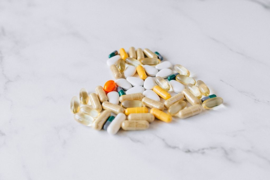 Heart shape made of various pills and capsules on a marble surface.