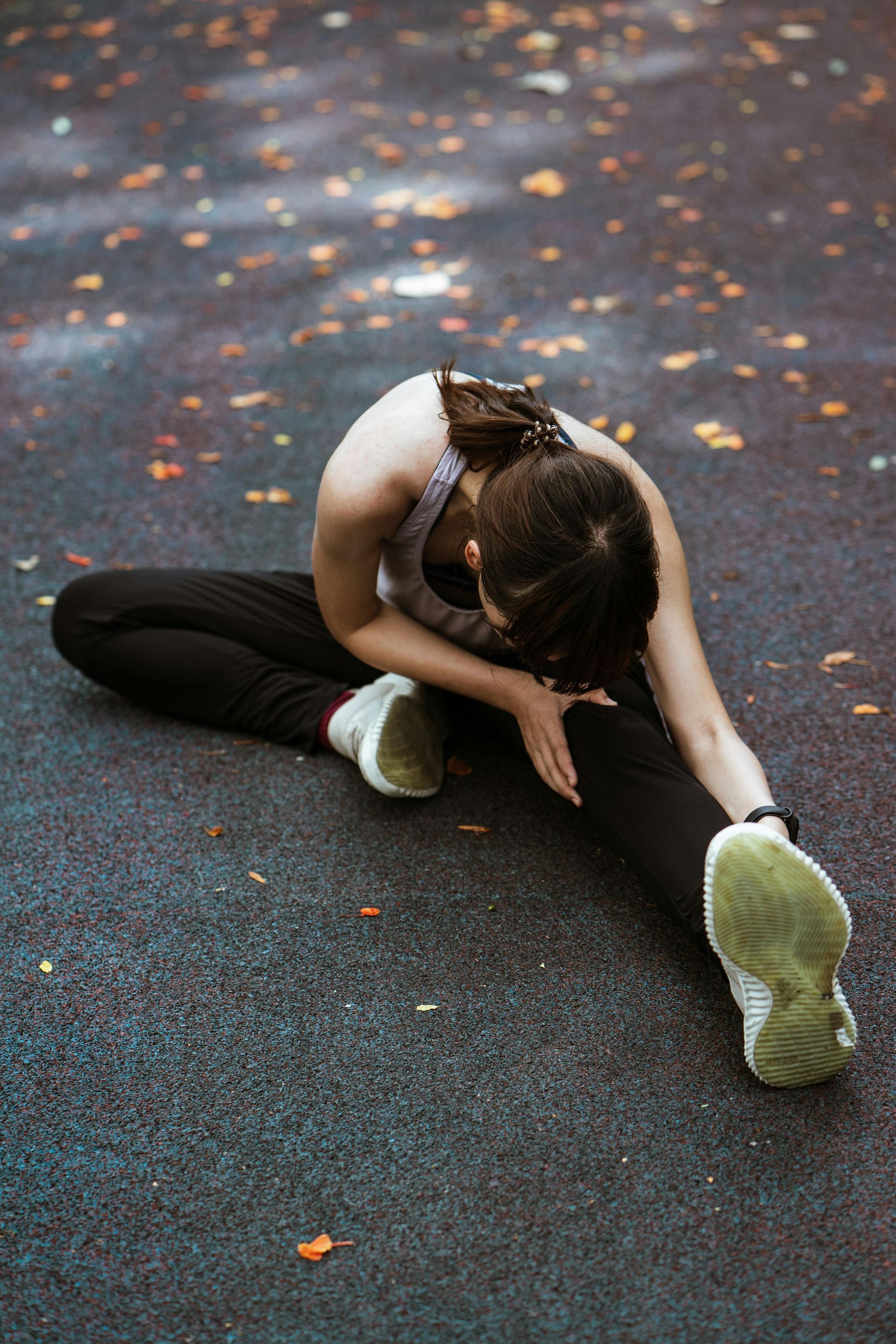 Woman stretching legs on ground, reaching for toes. Gray athletic wear in park.
