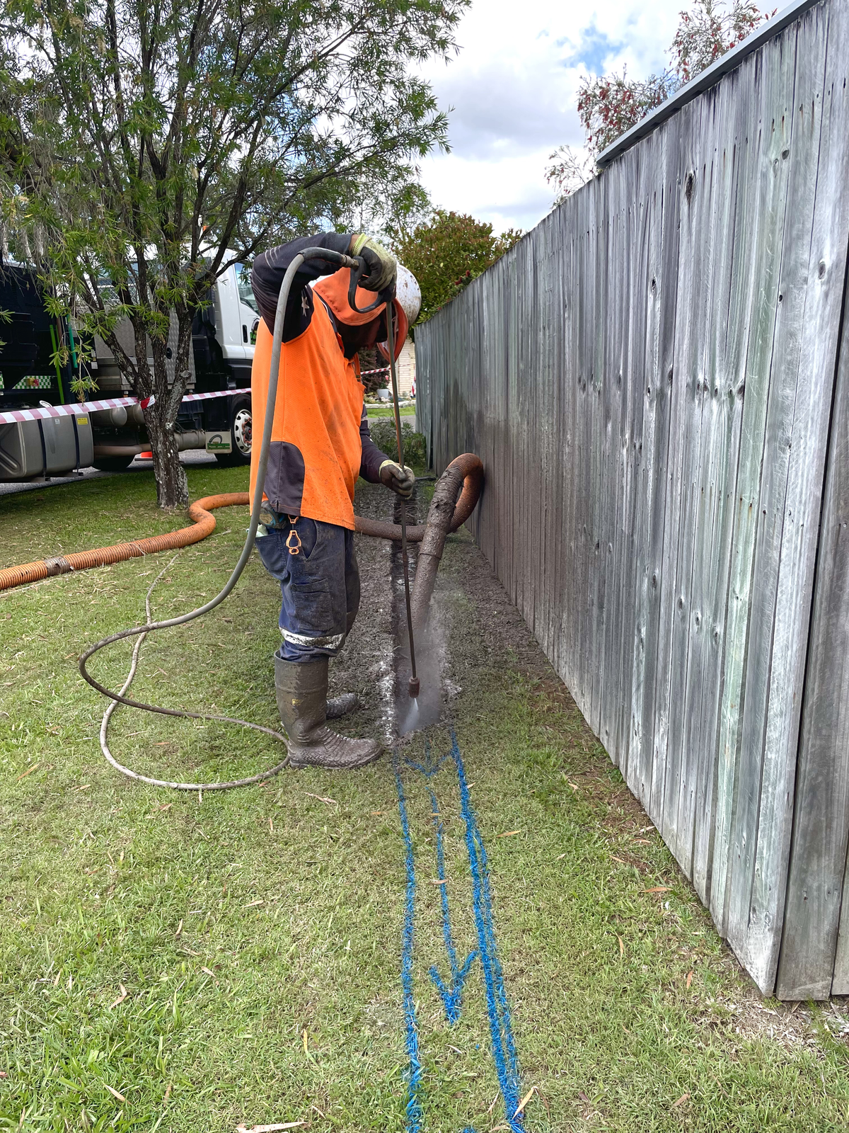 Worker in Orange Shirt Using Equipment Near a Wooden Fence and Grass — Tyzac Group in Beerwah, QLD