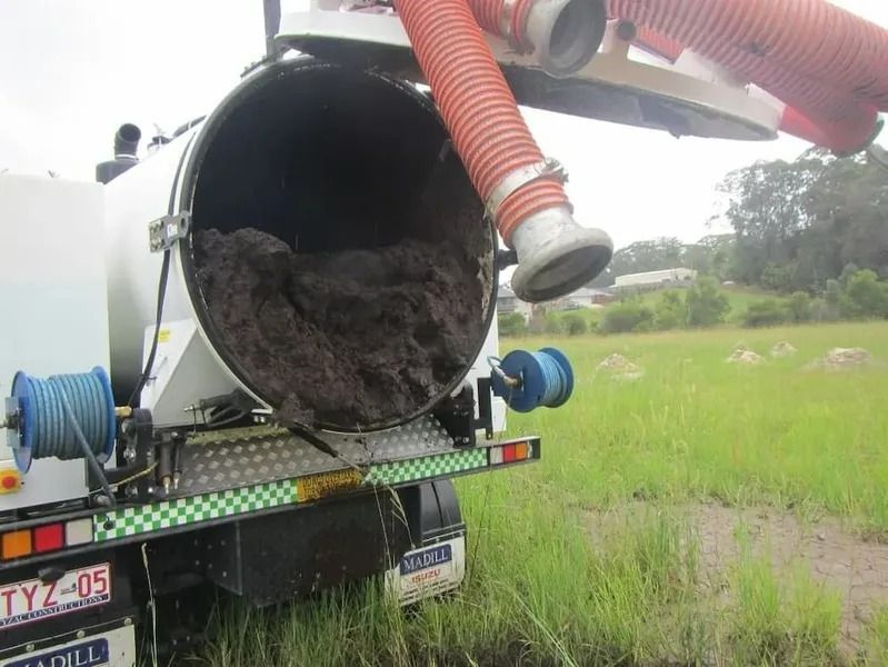 Truck With Open Tank Full of Sludge, Orange Hose Attached, in a Grassy Field — Tyzac Group in Beerwah, QLD