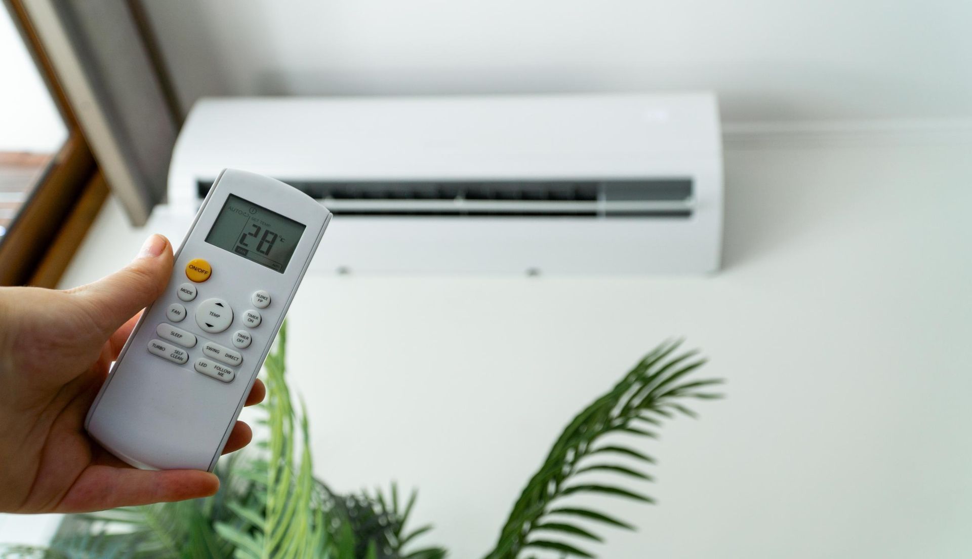 A person is holding a remote control in front of an air conditioner.