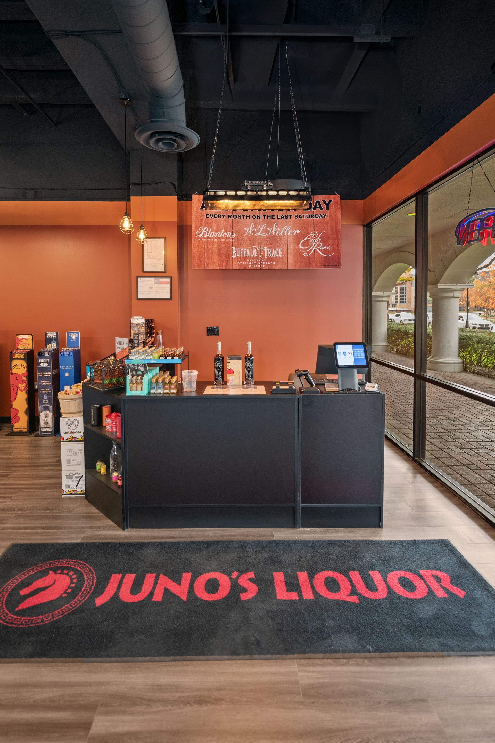 Juno's Liquor store interior with black counter, orange walls, and a welcome mat.