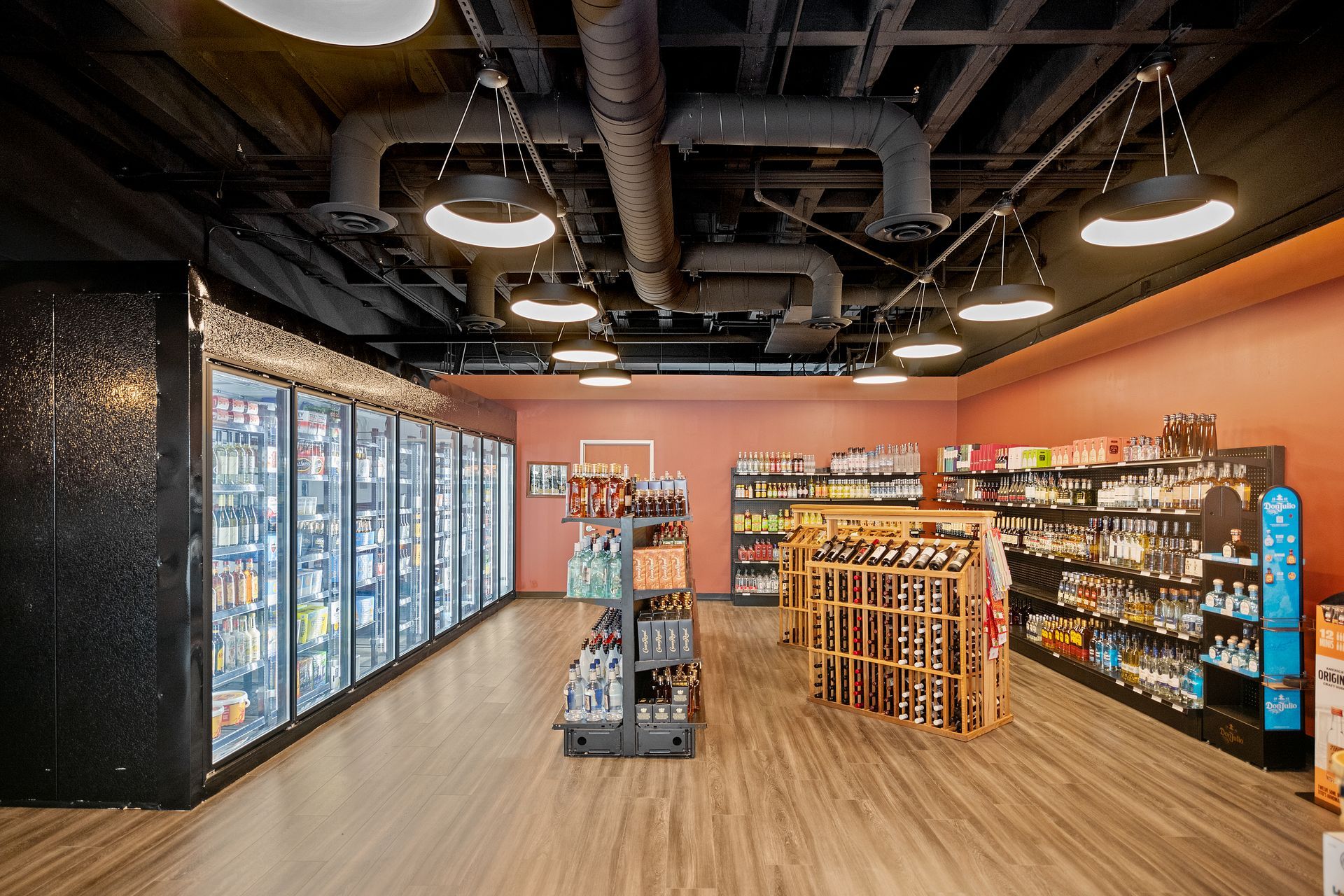 Interior of a liquor store with refrigerators, shelves of beverages, and wooden flooring.