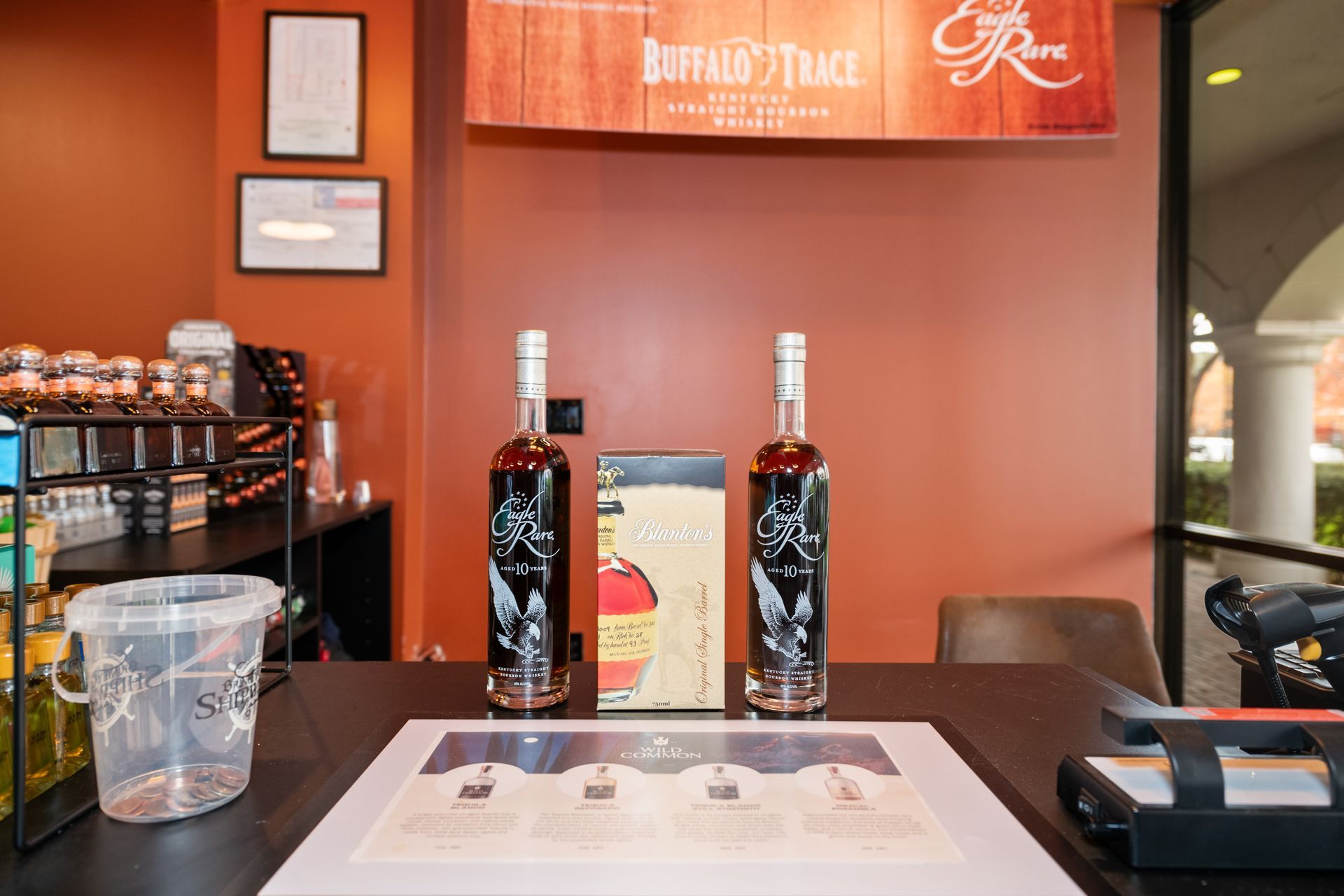 Two bottles of bourbon on a table, with a promotional display, inside a venue.