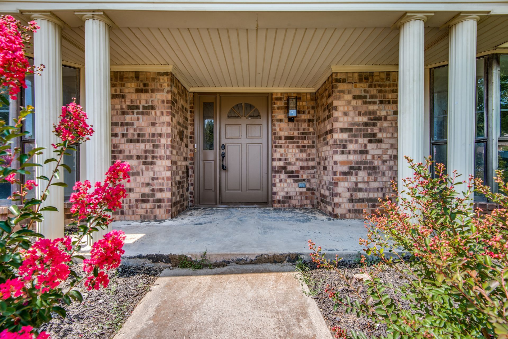 A brick house remodel with a porch and flowers in front of it