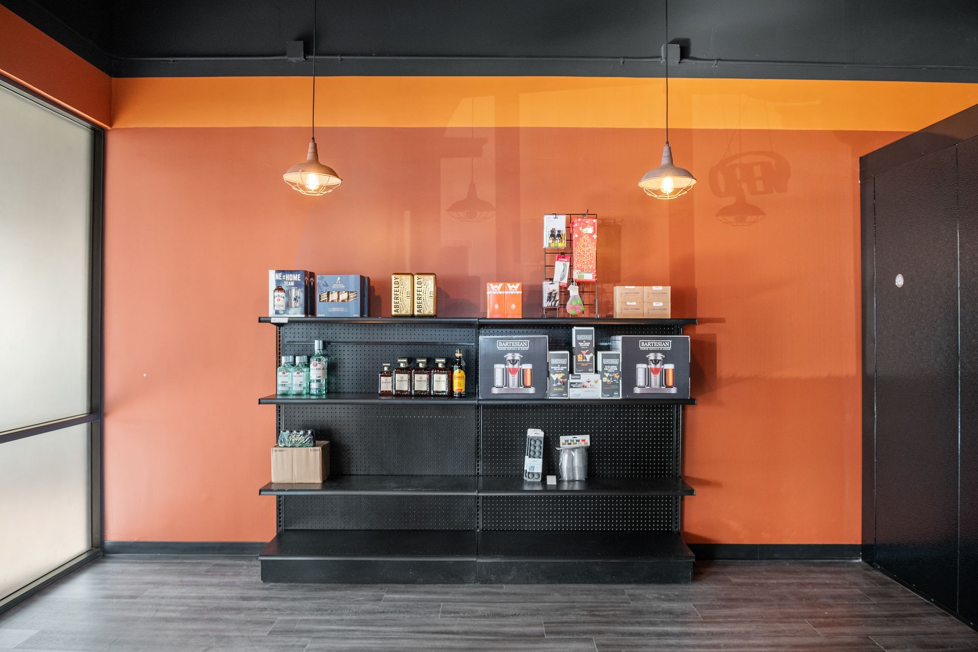 A retail display with shelves of products against an orange wall, under two pendant lights.