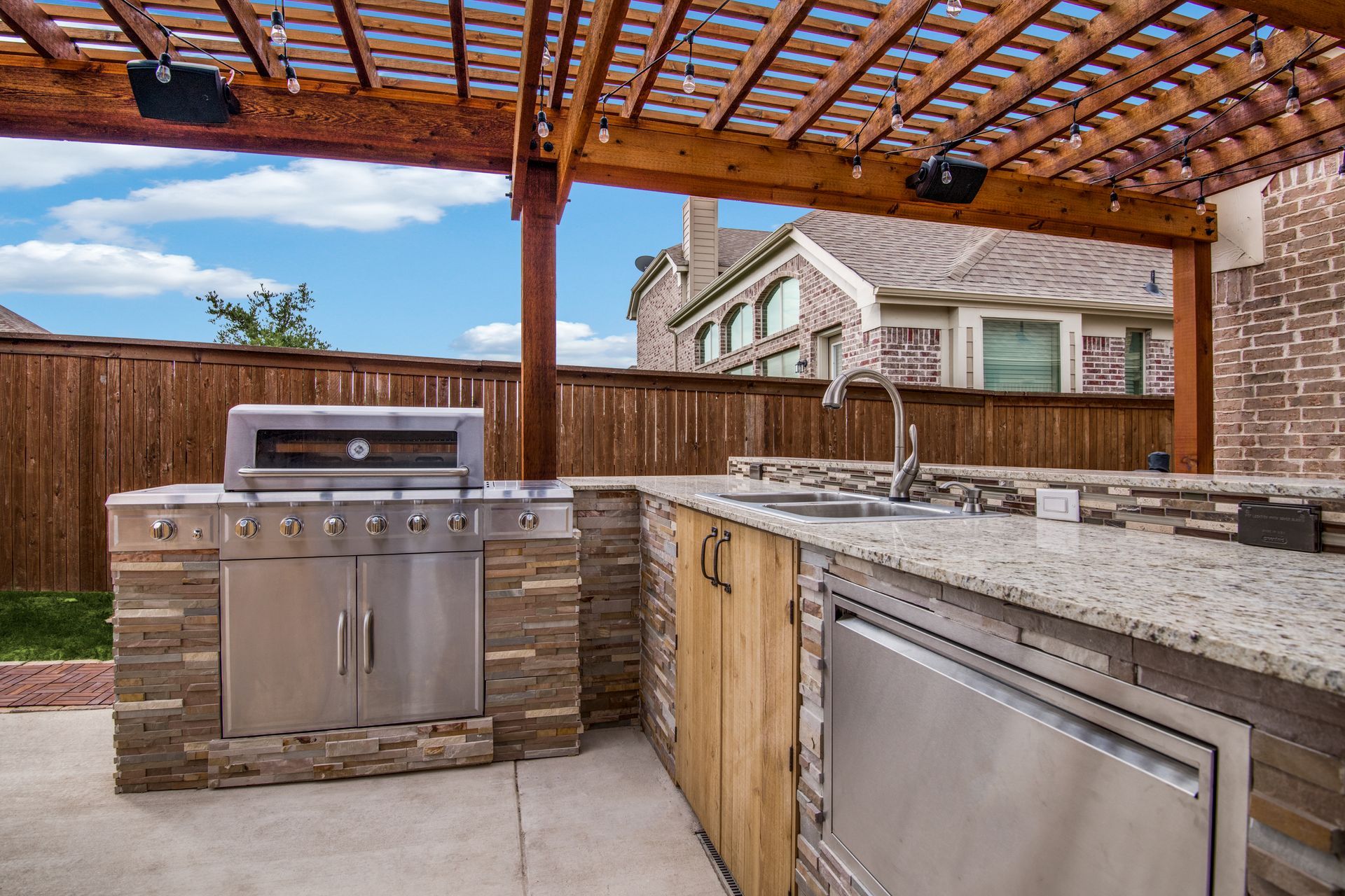 An outdoor kitchen remodel with a grill , sink , and pergola.