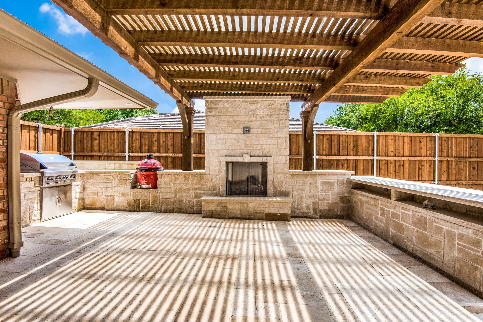 A patio remodel with a fireplace and a grill under a wooden pergola.