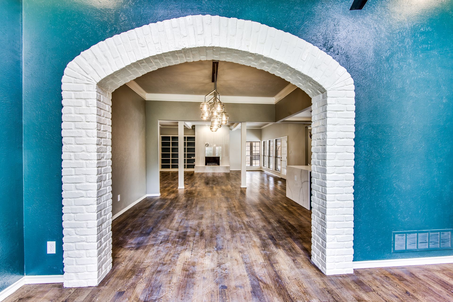 A Plano home remodel large empty room with a brick archway leading to a living room.