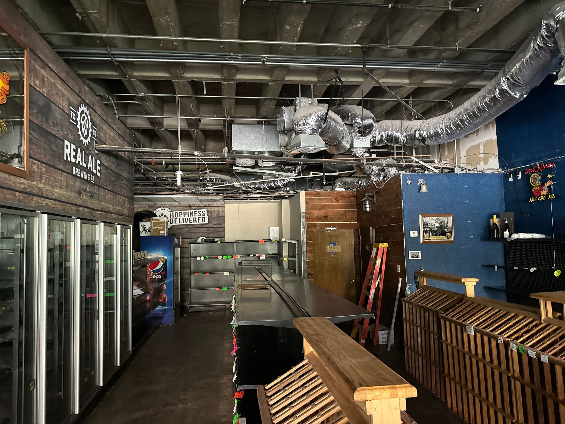 Interior view of a damaged business. Exposed ceiling, coolers, bar, and wooden crates are visible.