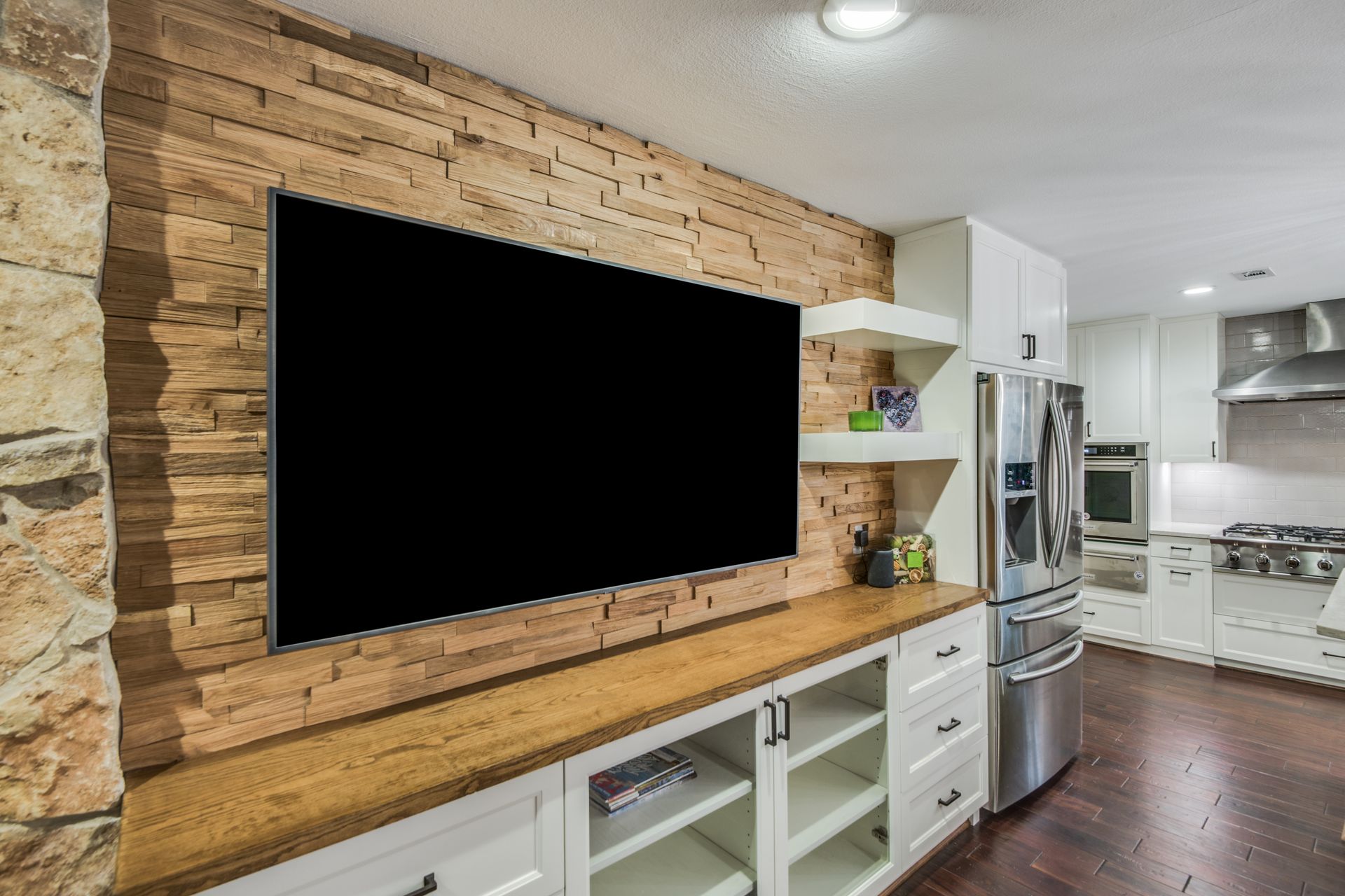 A large flat screen tv is mounted on a wooden wall in a kitchen.
