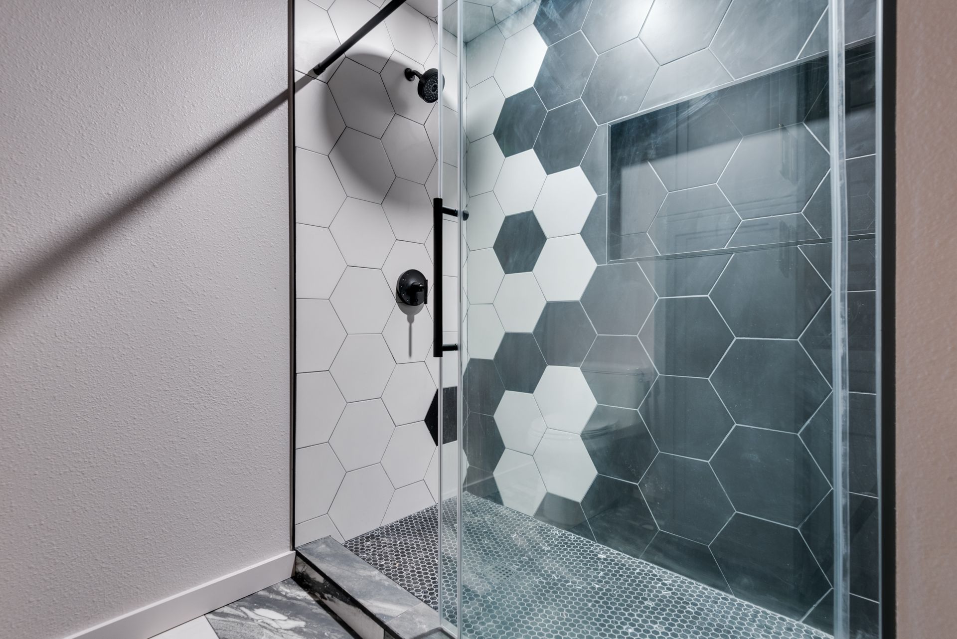 A shower remodel with black and white hexagon tiles and a glass door.