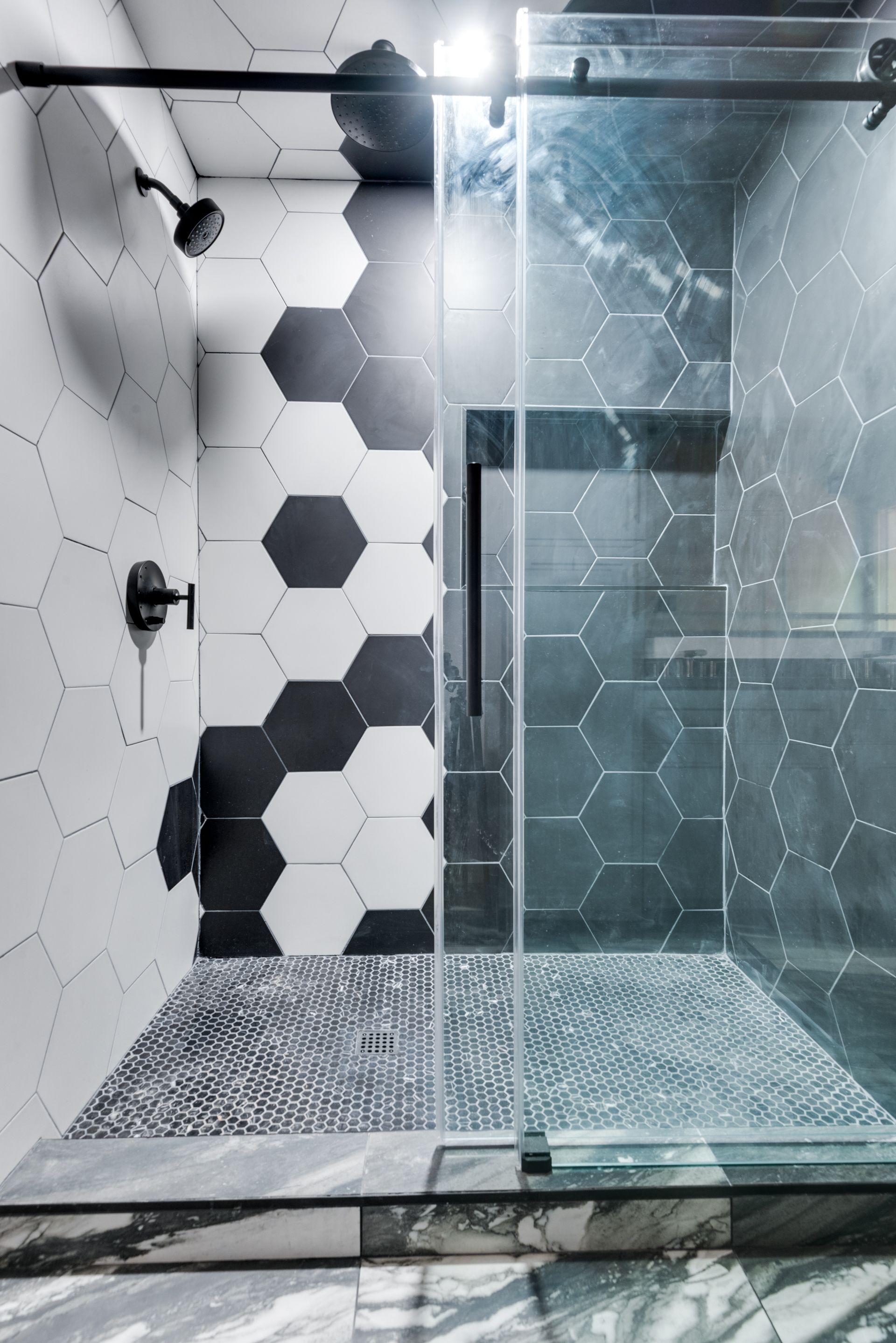A bathroom remodel with black and white tiles and a walk in shower.