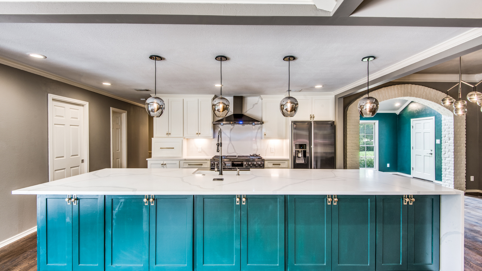 Modern kitchen with teal island, white countertops, pendant lights, and white cabinets.