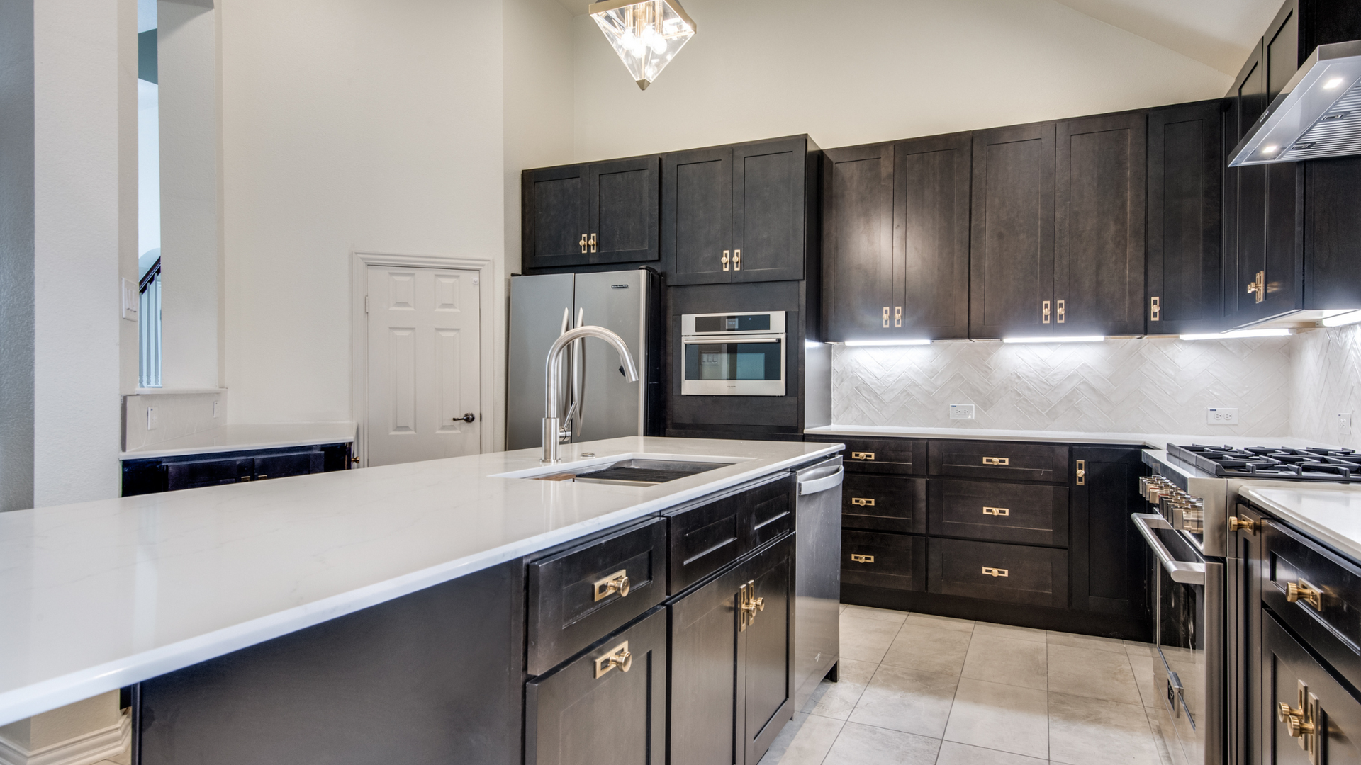 Modern kitchen with dark cabinets, stainless steel appliances, and a white countertop island.