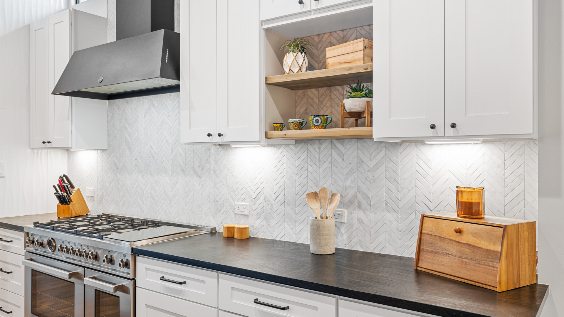Bright kitchen with white cabinets, black countertops, and a stainless steel stove.