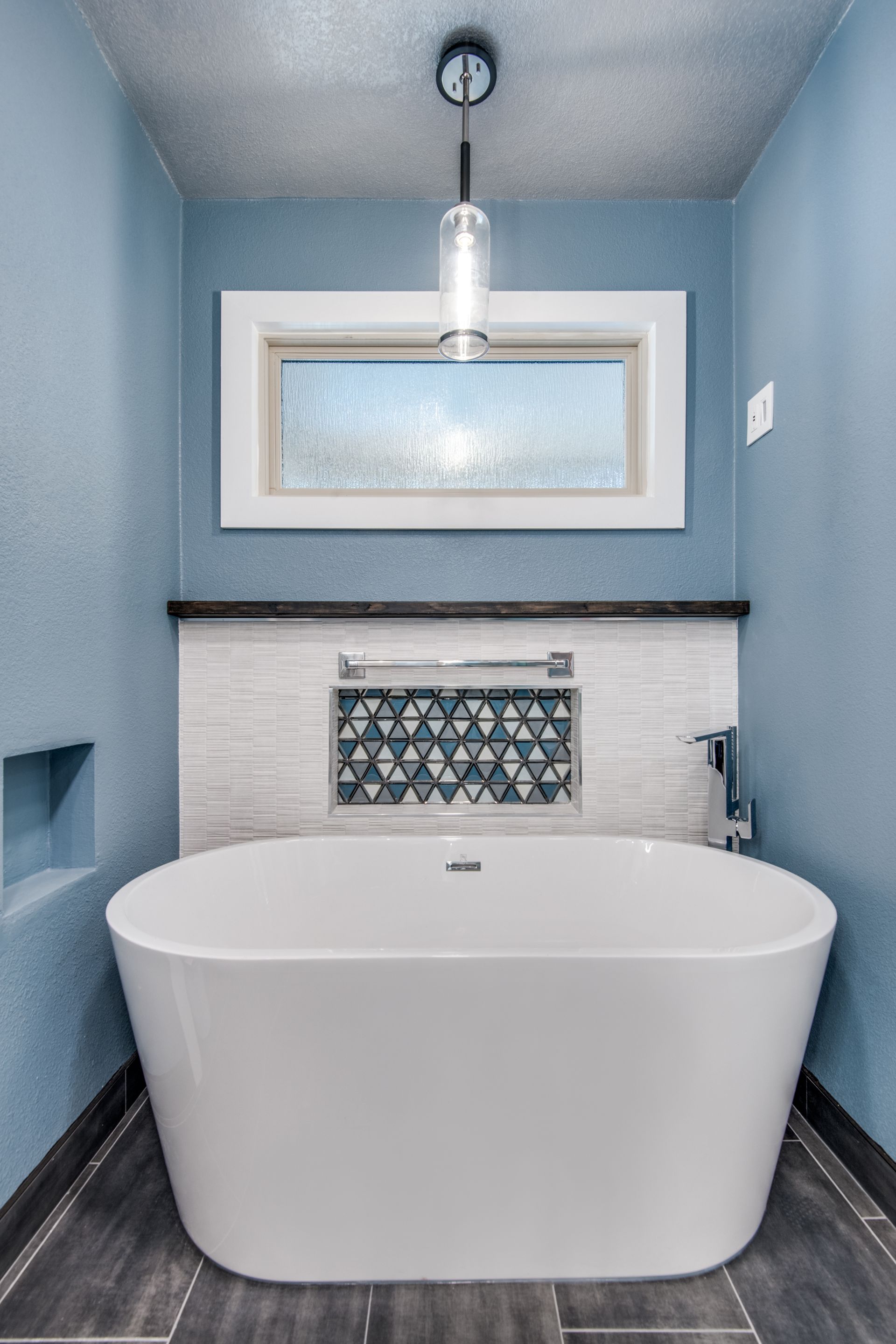 A bathtub remodel in a bathroom with blue walls and a window.
