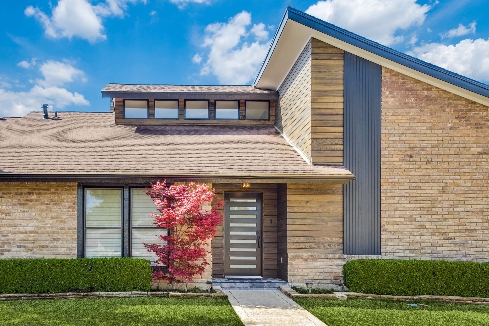 A brick house remodel with a blue roof and a tree in front of it.