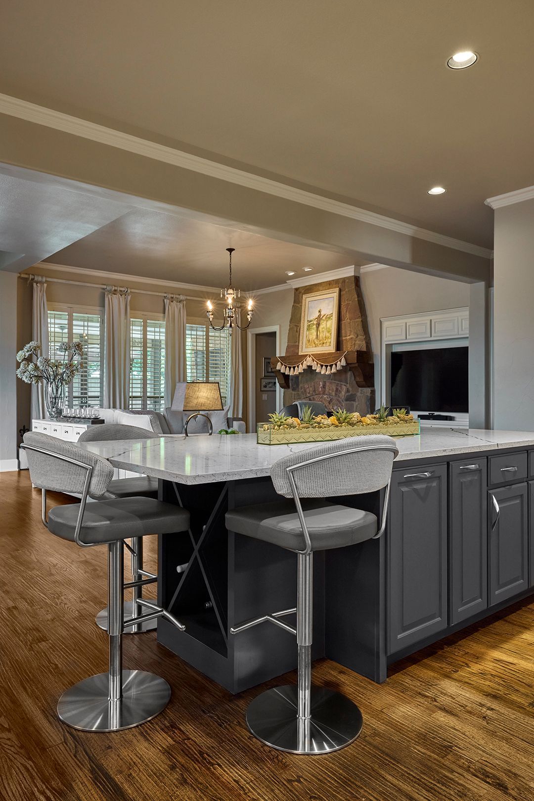 A kitchen with a large island and stools and a living room in the background.