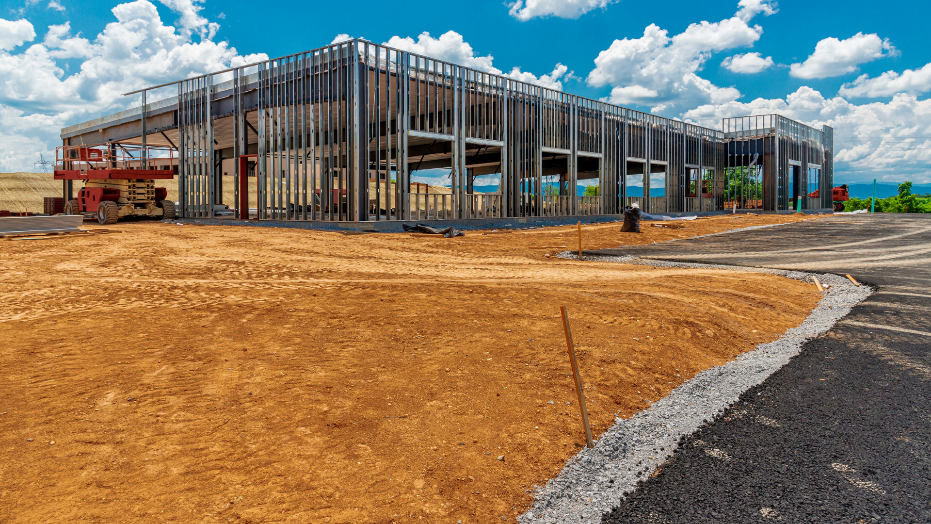 Steel frame of a building under construction with earth moving equipment against a blue sky.
