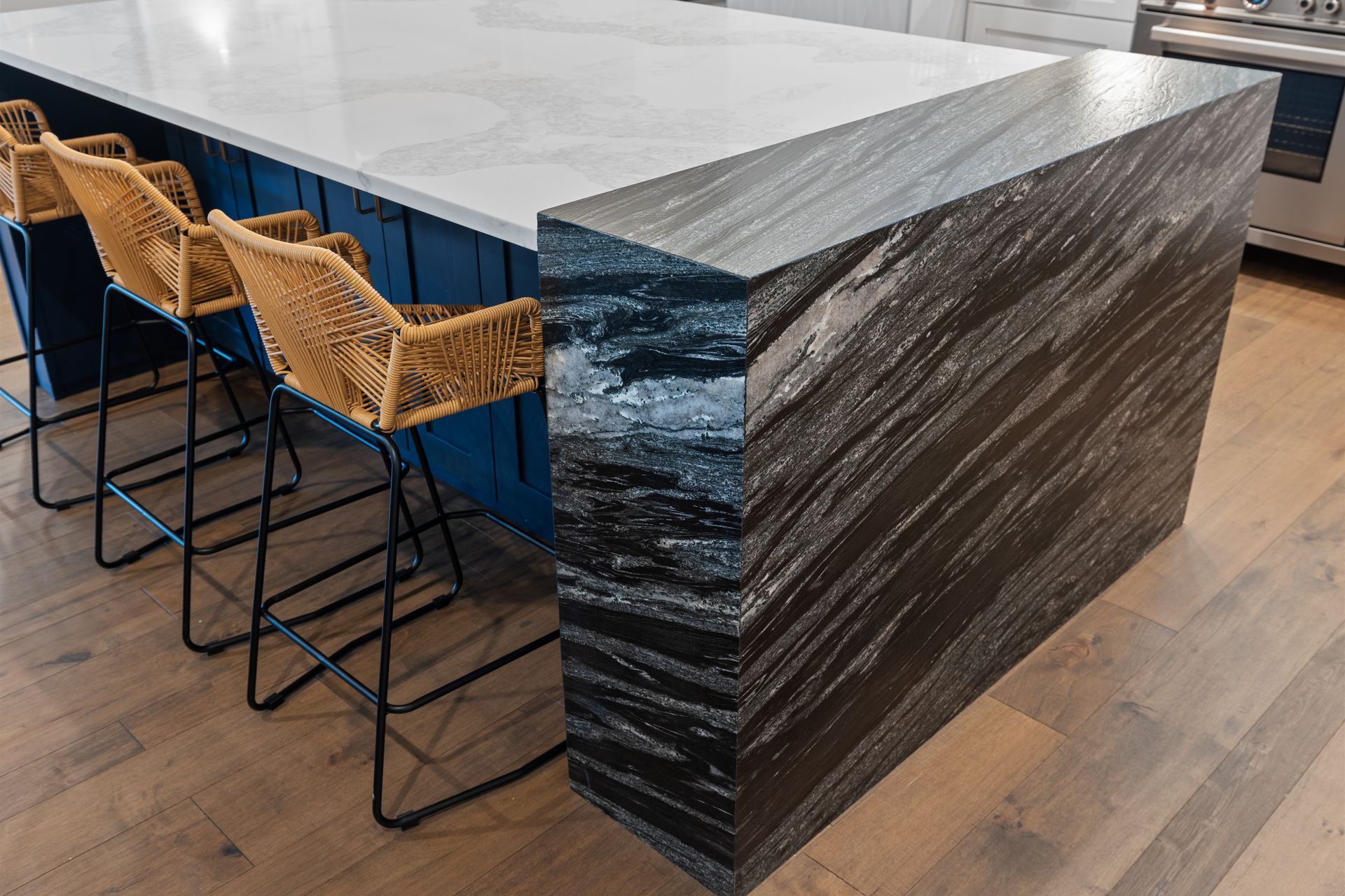 A kitchen island with wicker chairs and a granite counter top.