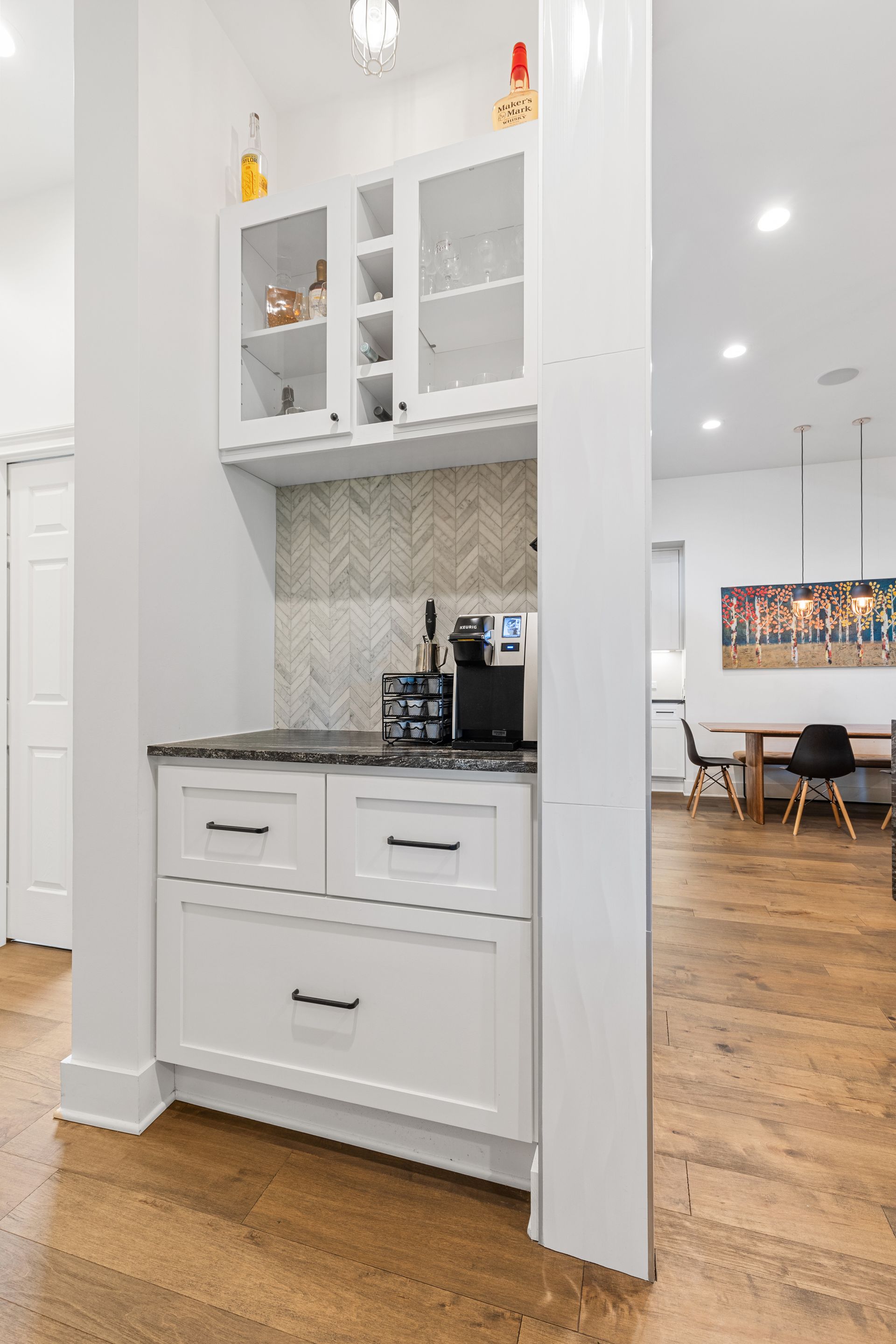 A kitchen with white cabinets and hardwood floors and a bar.