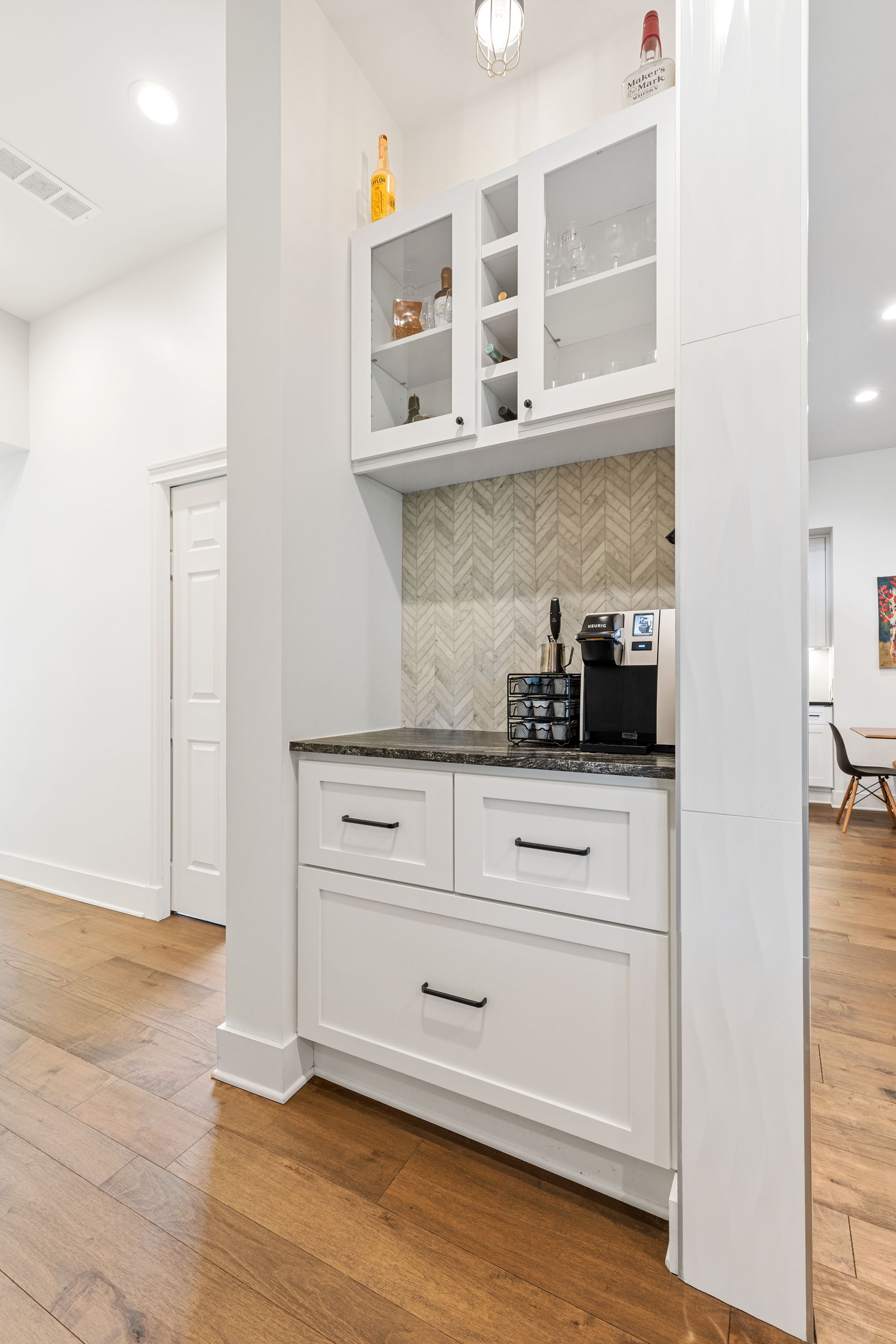A kitchen with white cabinets and hardwood floors and a coffee maker.
