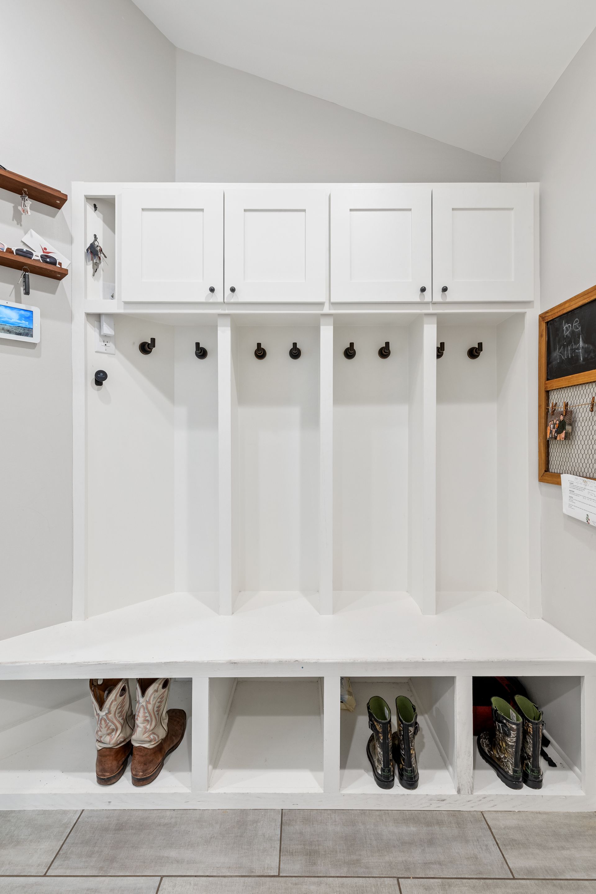 A mud room with a bench , shelves , hooks and a chalkboard.