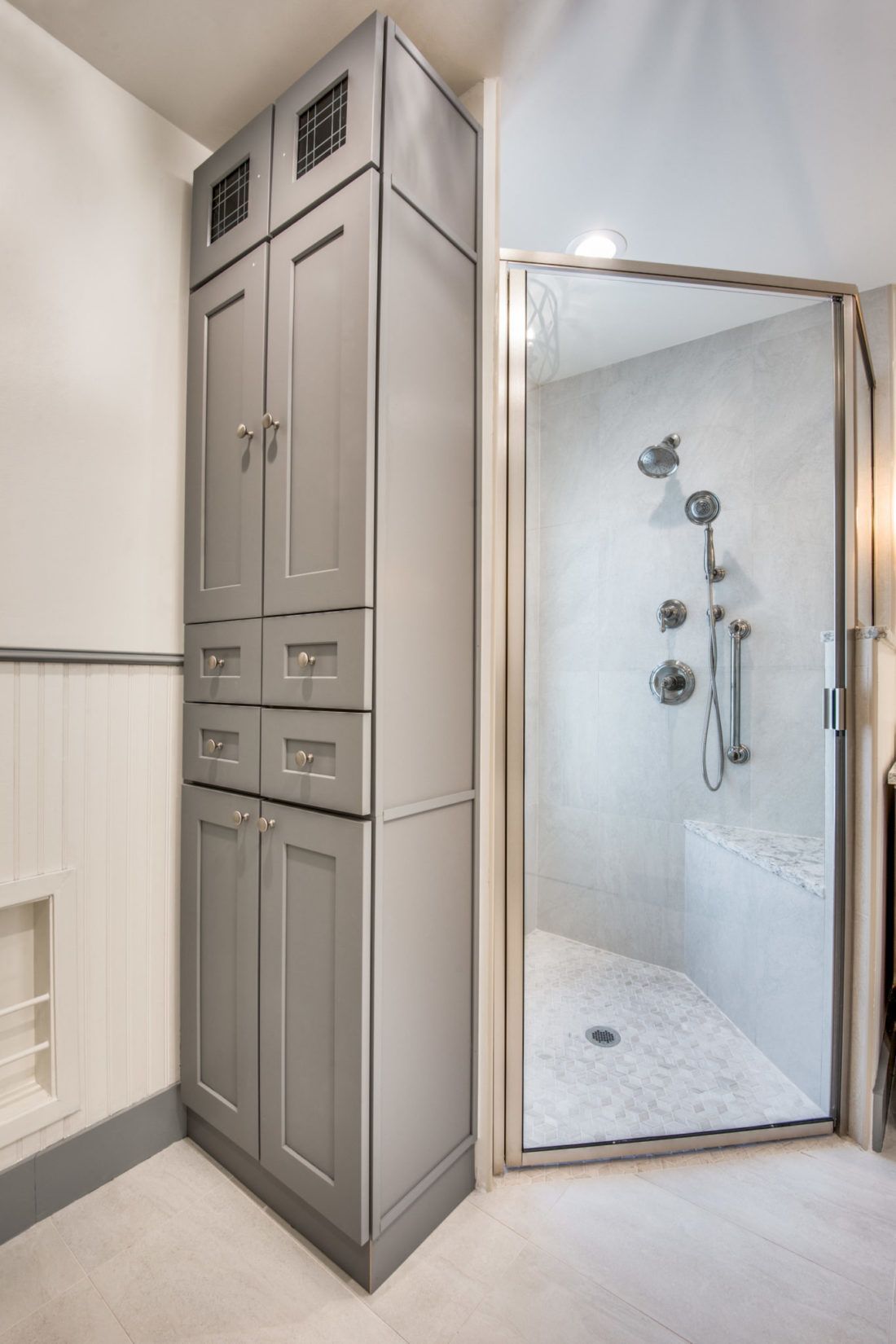 A bathroom with gray cabinets and a walk in shower.