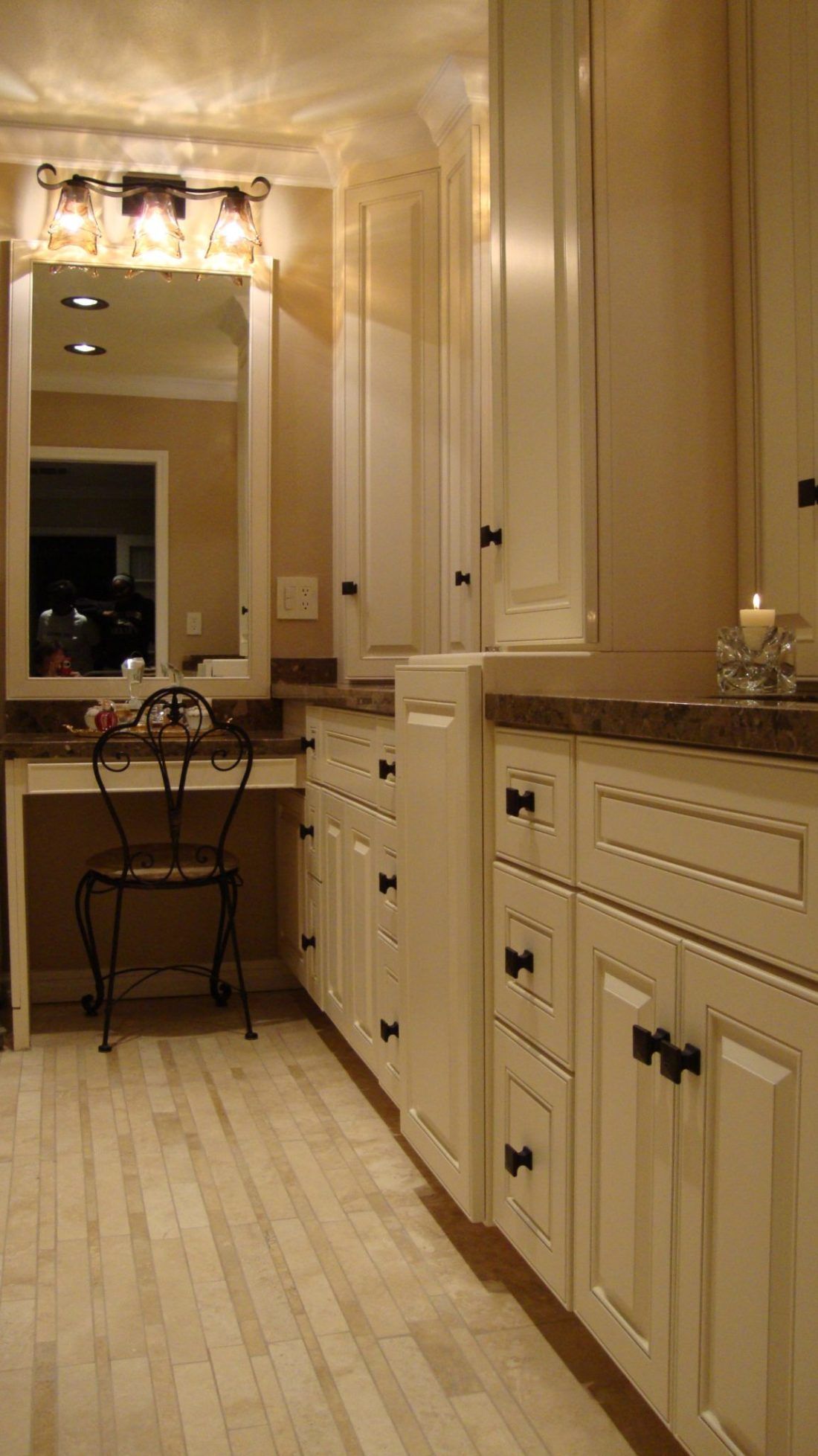 A bathroom with white cabinets , a vanity , a mirror and a chair.