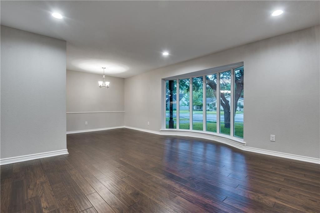 An empty living room with hardwood floors and large windows.