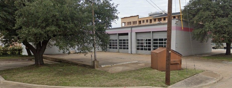 A fire station is sitting on the corner of a street next to a tree.