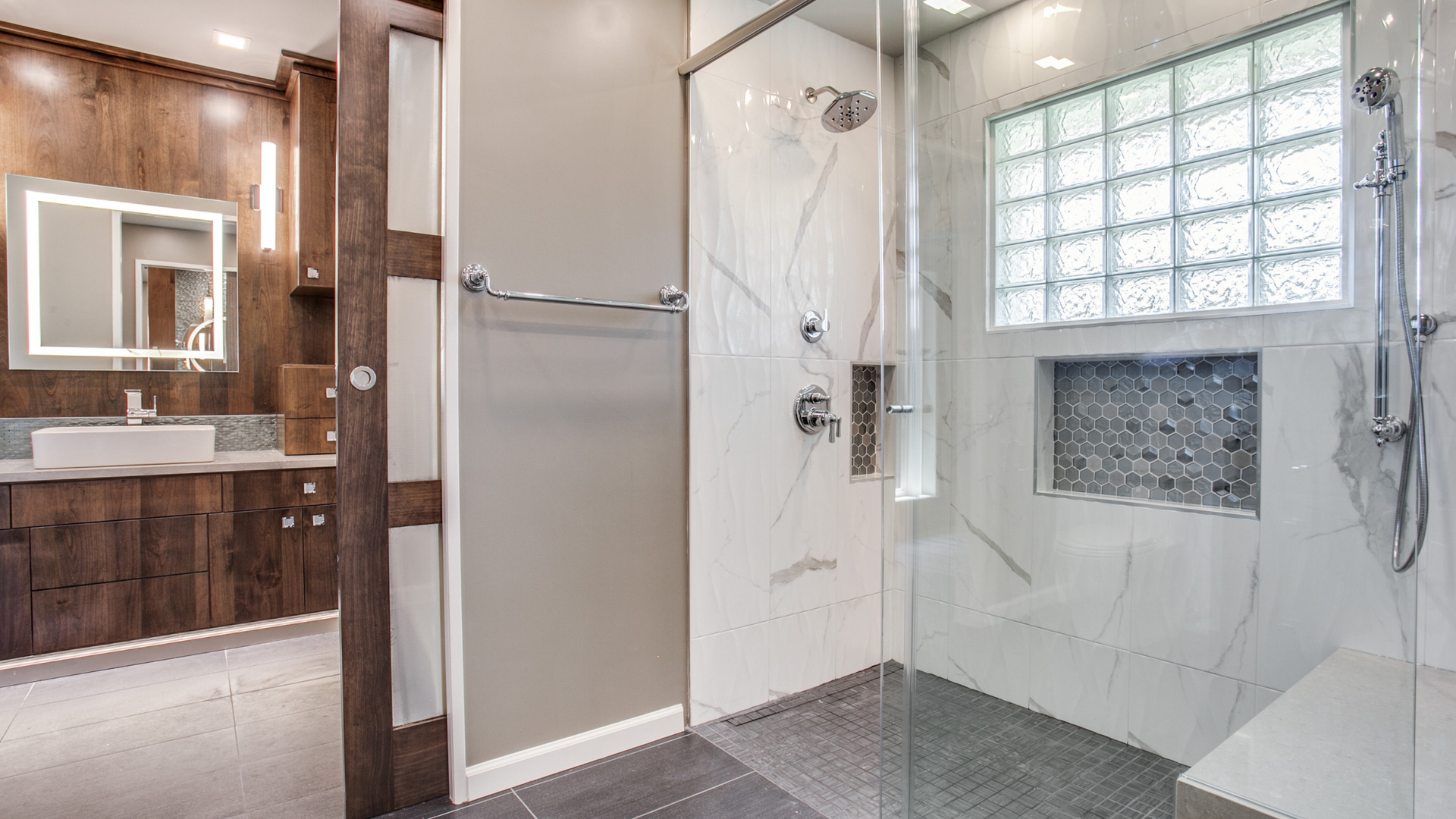 Modern bathroom with marble shower, glass block window, and wood vanity.