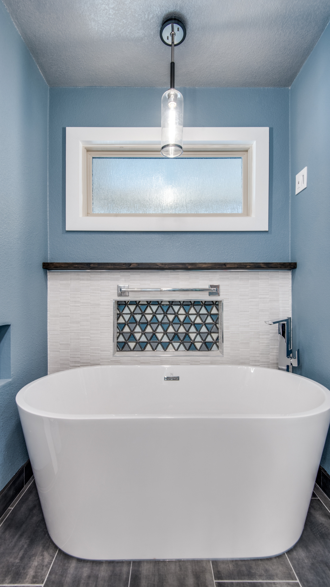 Blue bathroom with a white soaking tub, mosaic tile accents, and a window.