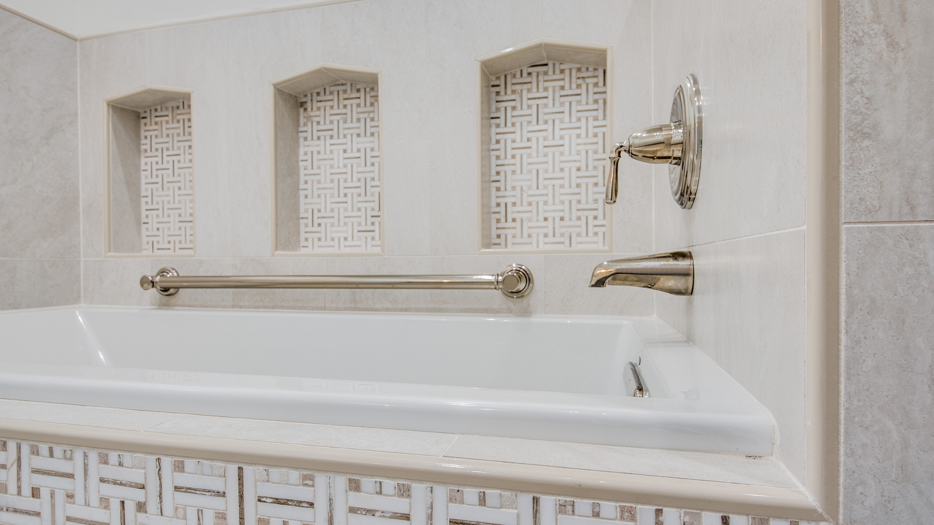 White bathtub with grab bar and decorative niches in a tiled bathroom.