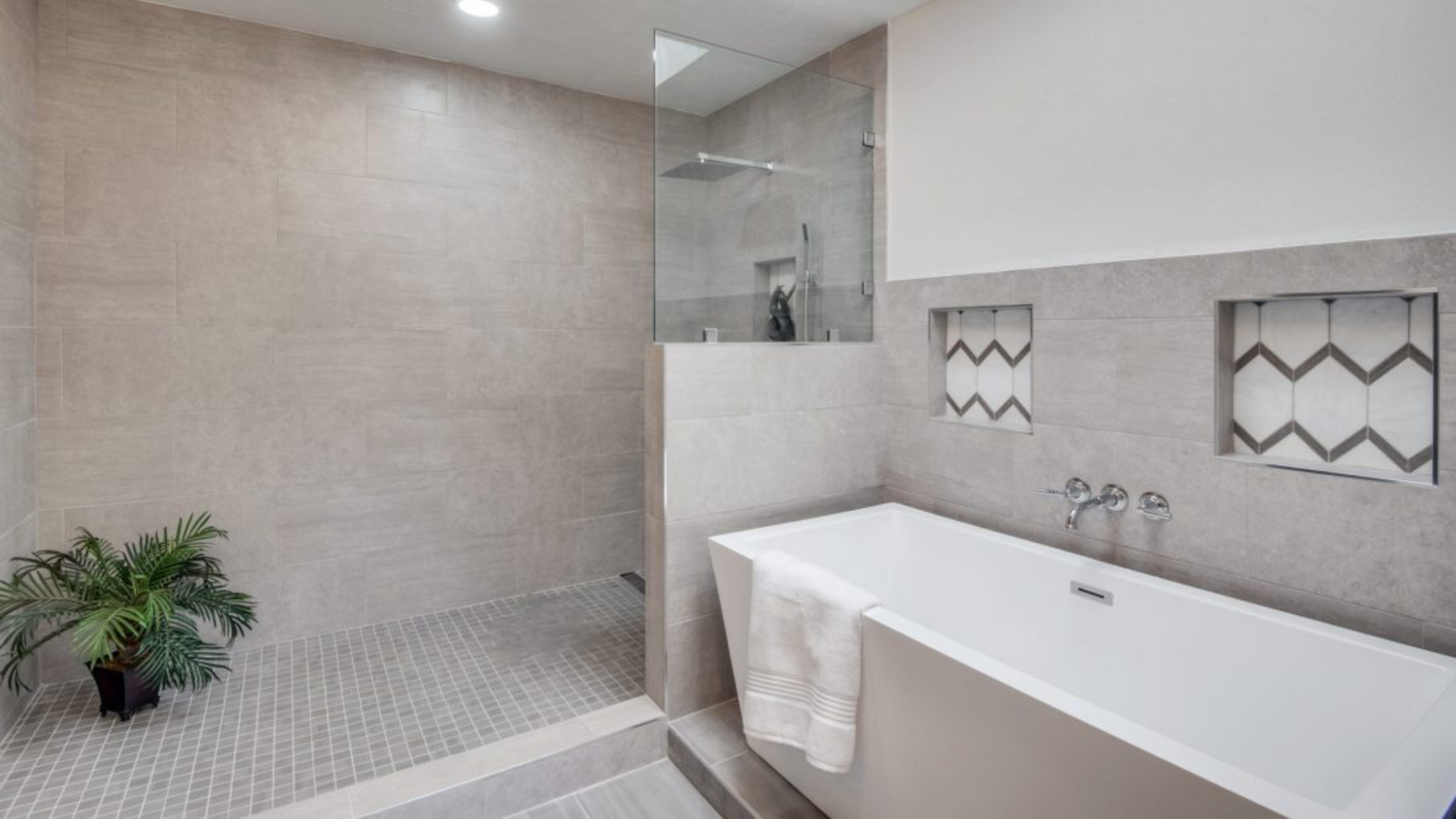 Modern bathroom with grey tiling, a soaking tub, and a walk-in shower with a small plant.