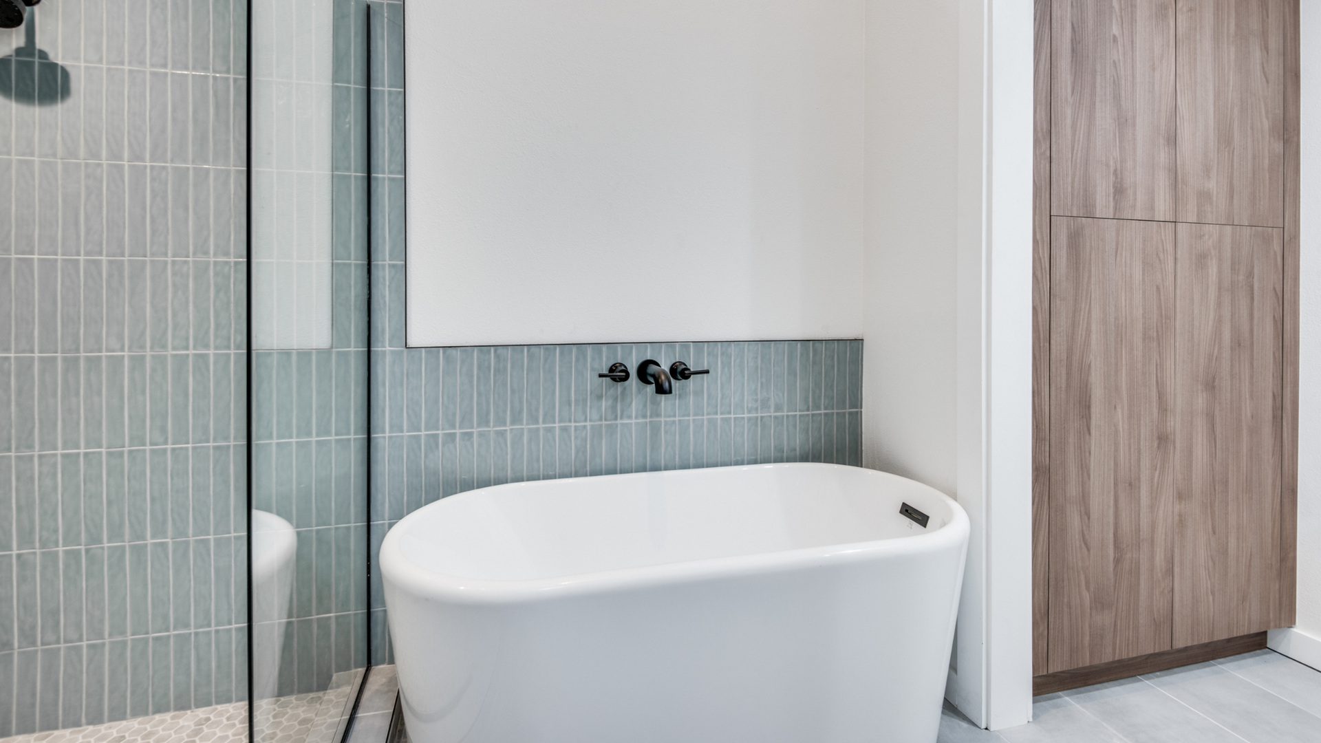 Modern bathroom with white tub, blue tile, and light wood cabinet.
