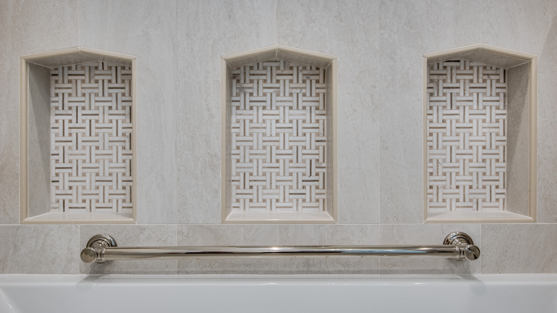 Three recessed tiled niches above a bathtub, with a chrome towel bar.