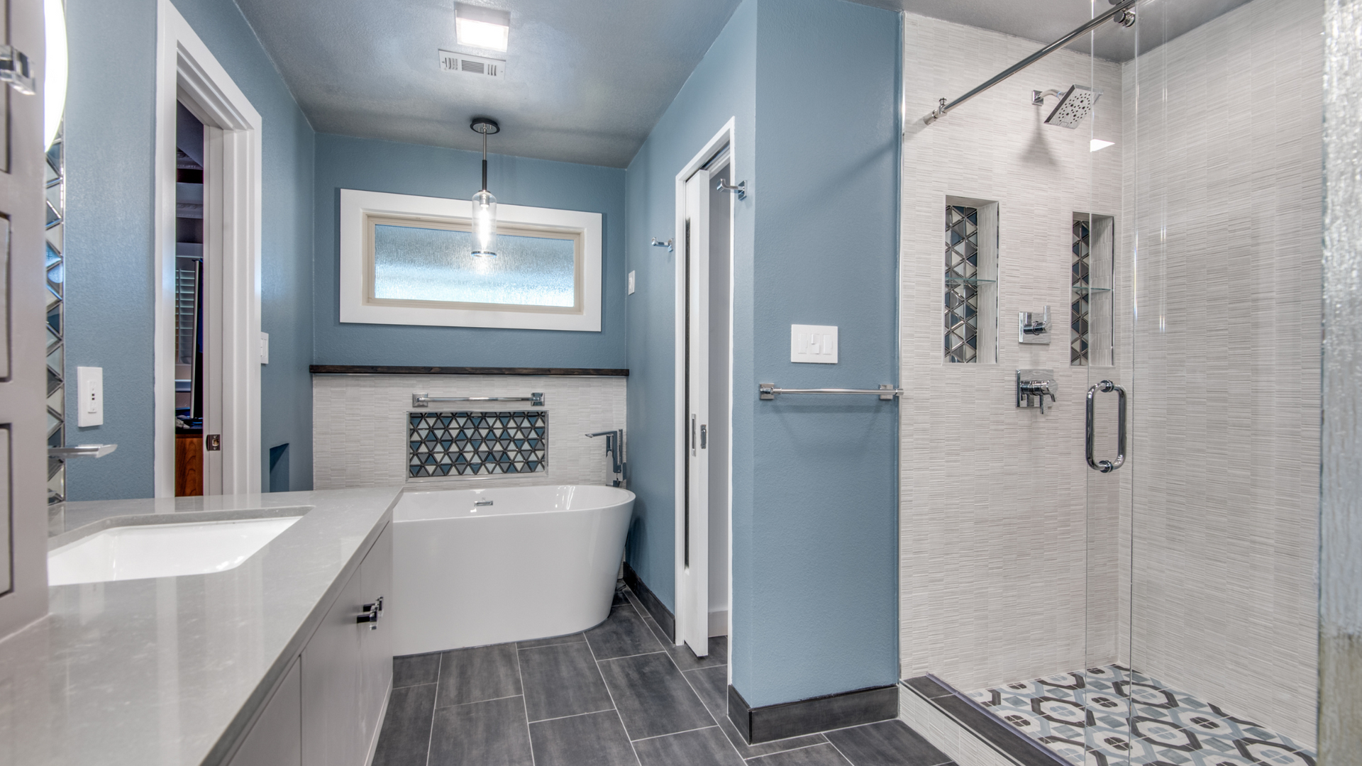 Blue bathroom with a white soaking tub, glass shower, and modern fixtures.