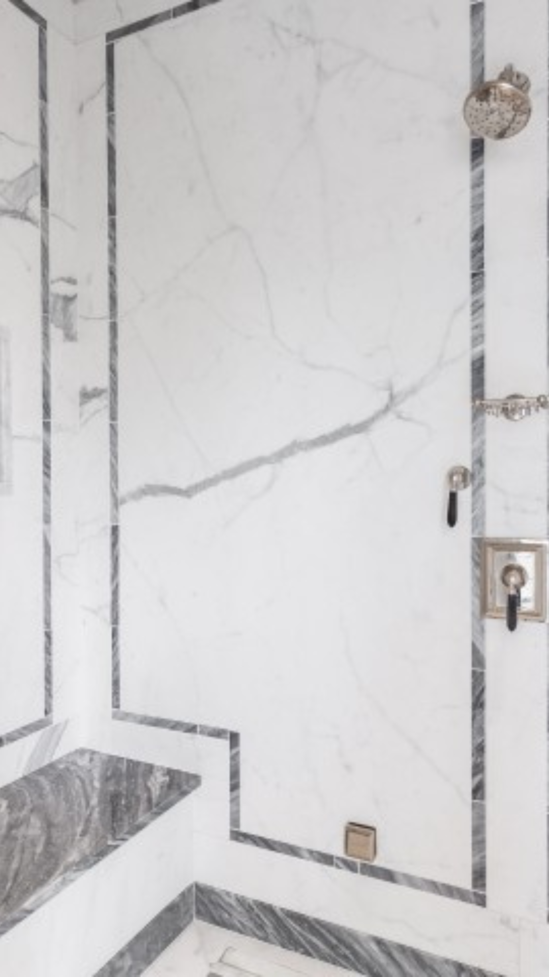 White marble shower with gray veining, black trim, silver fixtures.