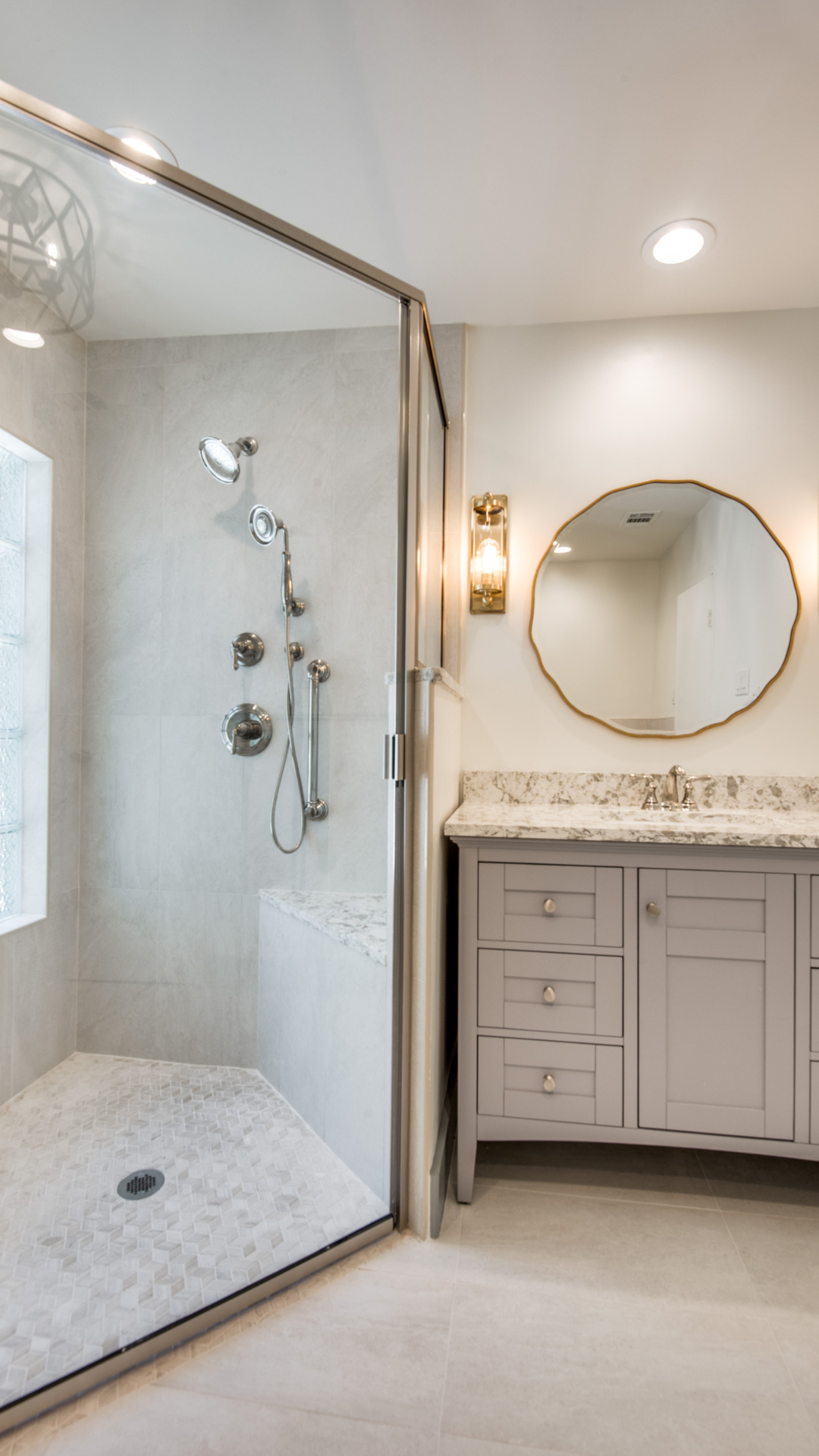 Modern bathroom with glass shower, gray vanity, and round gold mirror.