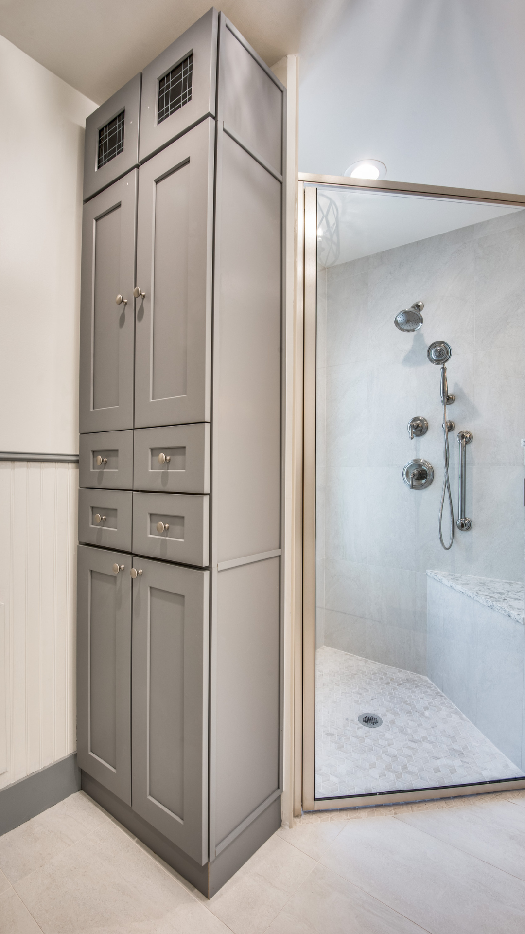 Tall gray storage cabinet next to a glass-doored shower in a bathroom.