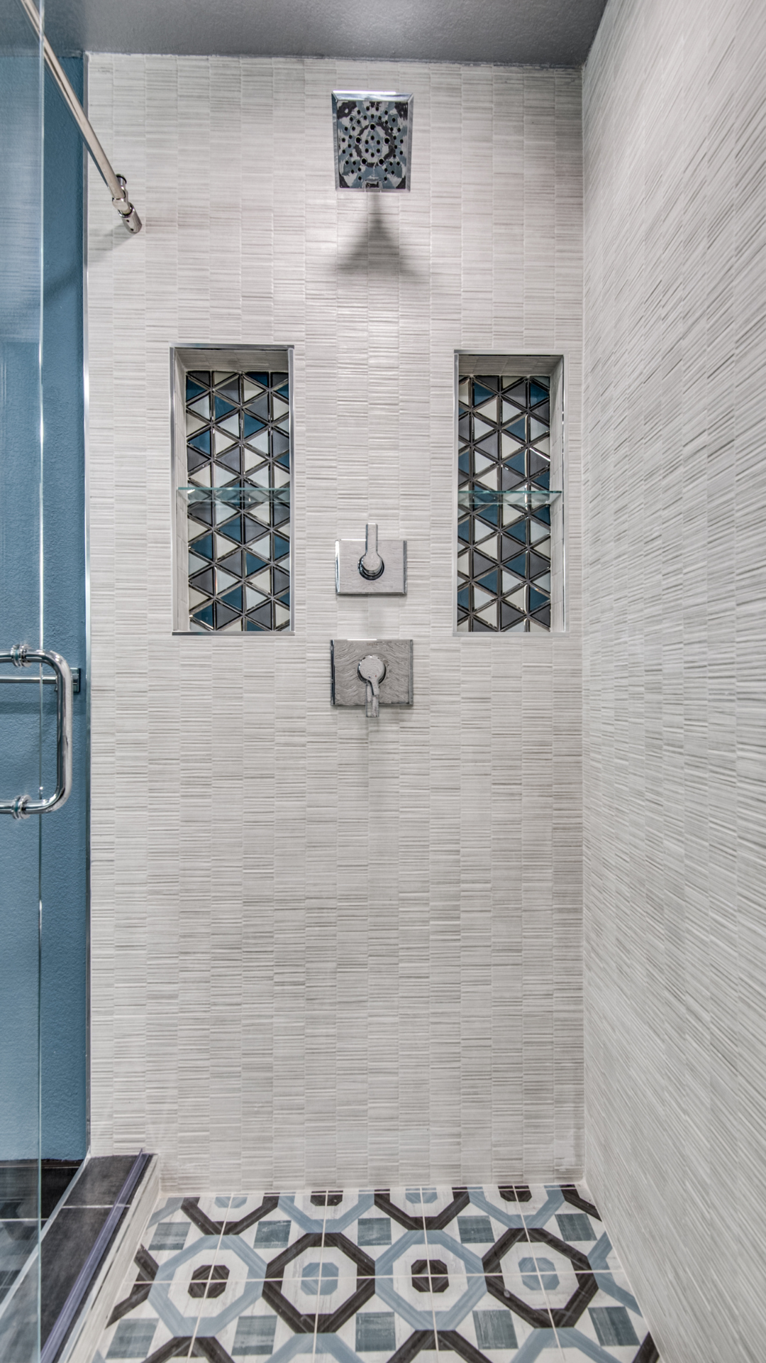 Shower with white textured walls, patterned floor, and blue and gray accents.