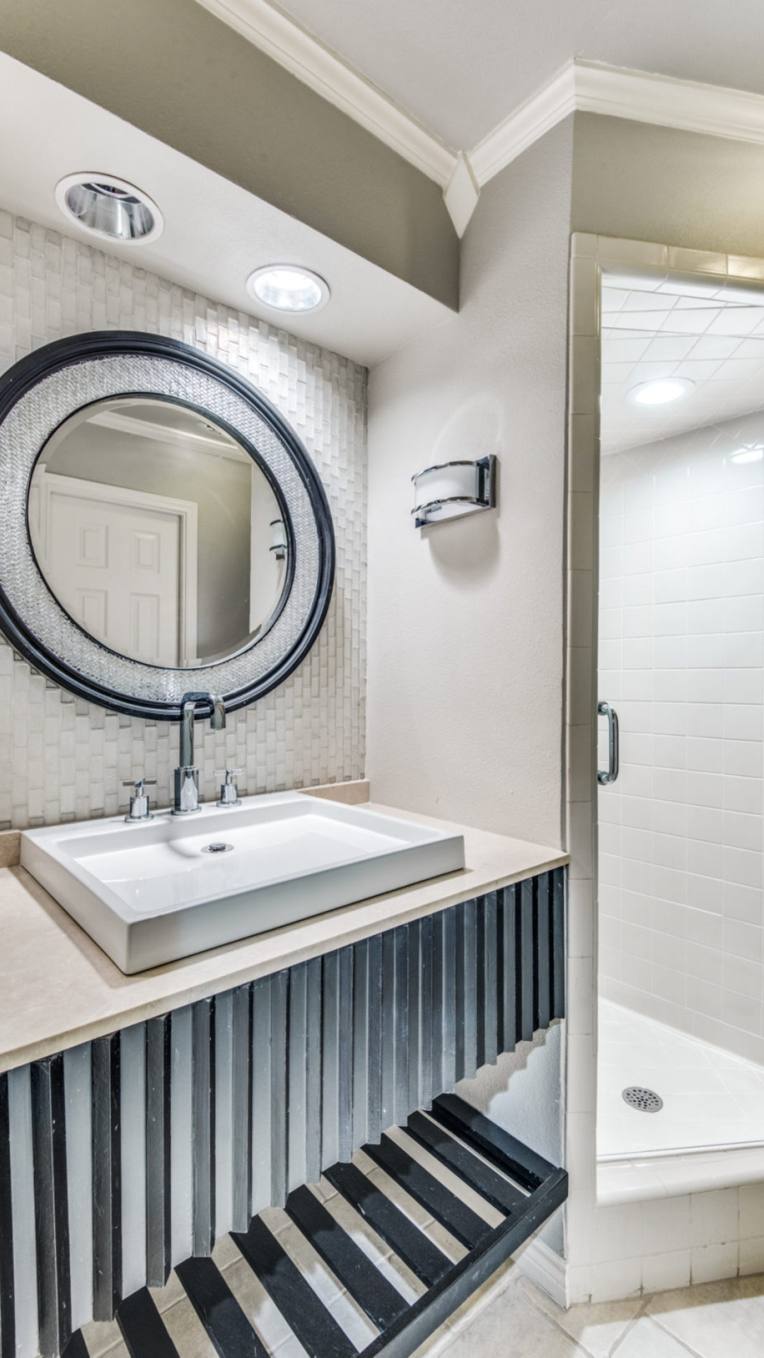 Bathroom with a floating vanity, a round mirror, and a glass-door shower.