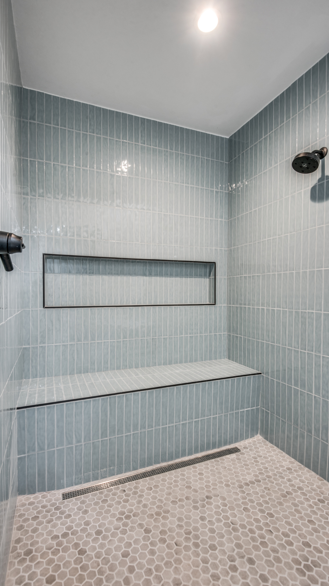 Shower with blue tiled walls, built-in bench, and gray hexagon floor tiles. Black fixtures.