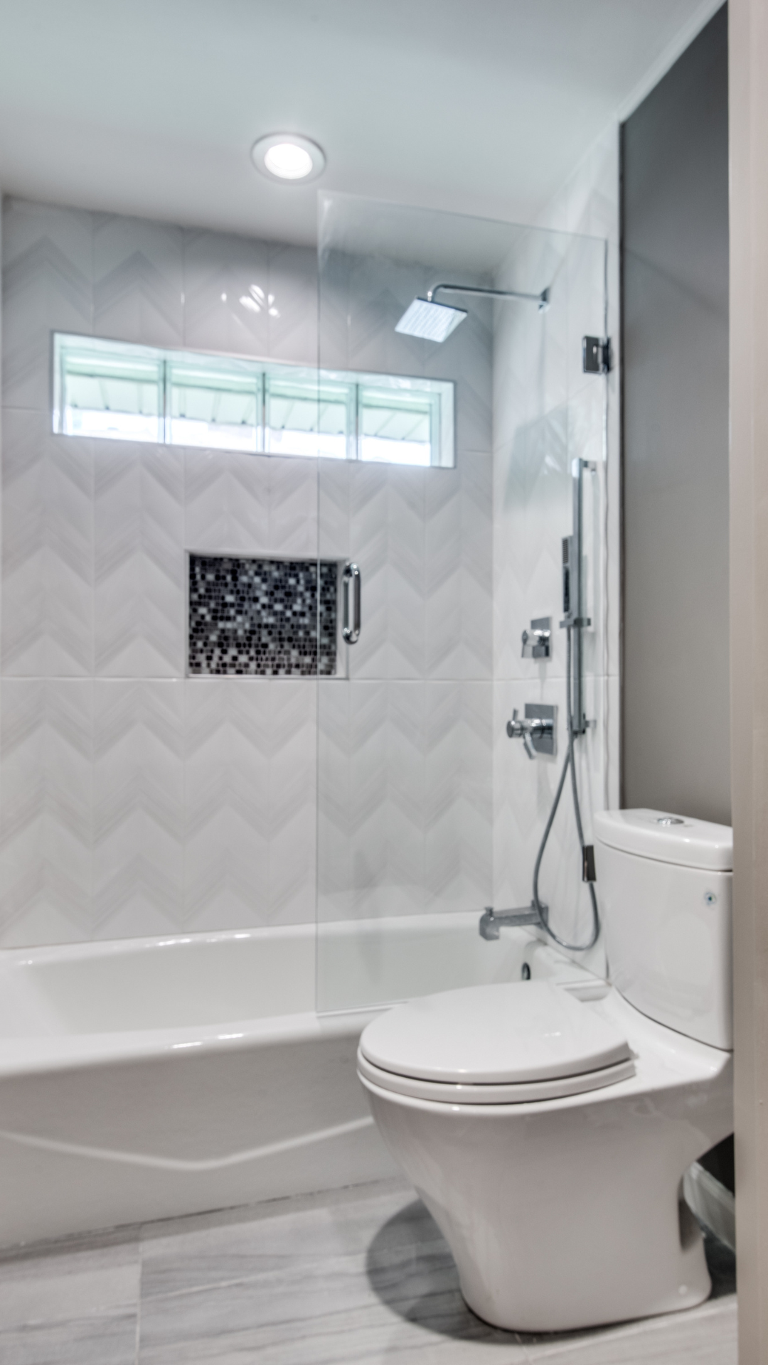 Modern bathroom with white toilet, tub, and patterned tile. Glass shower enclosure.