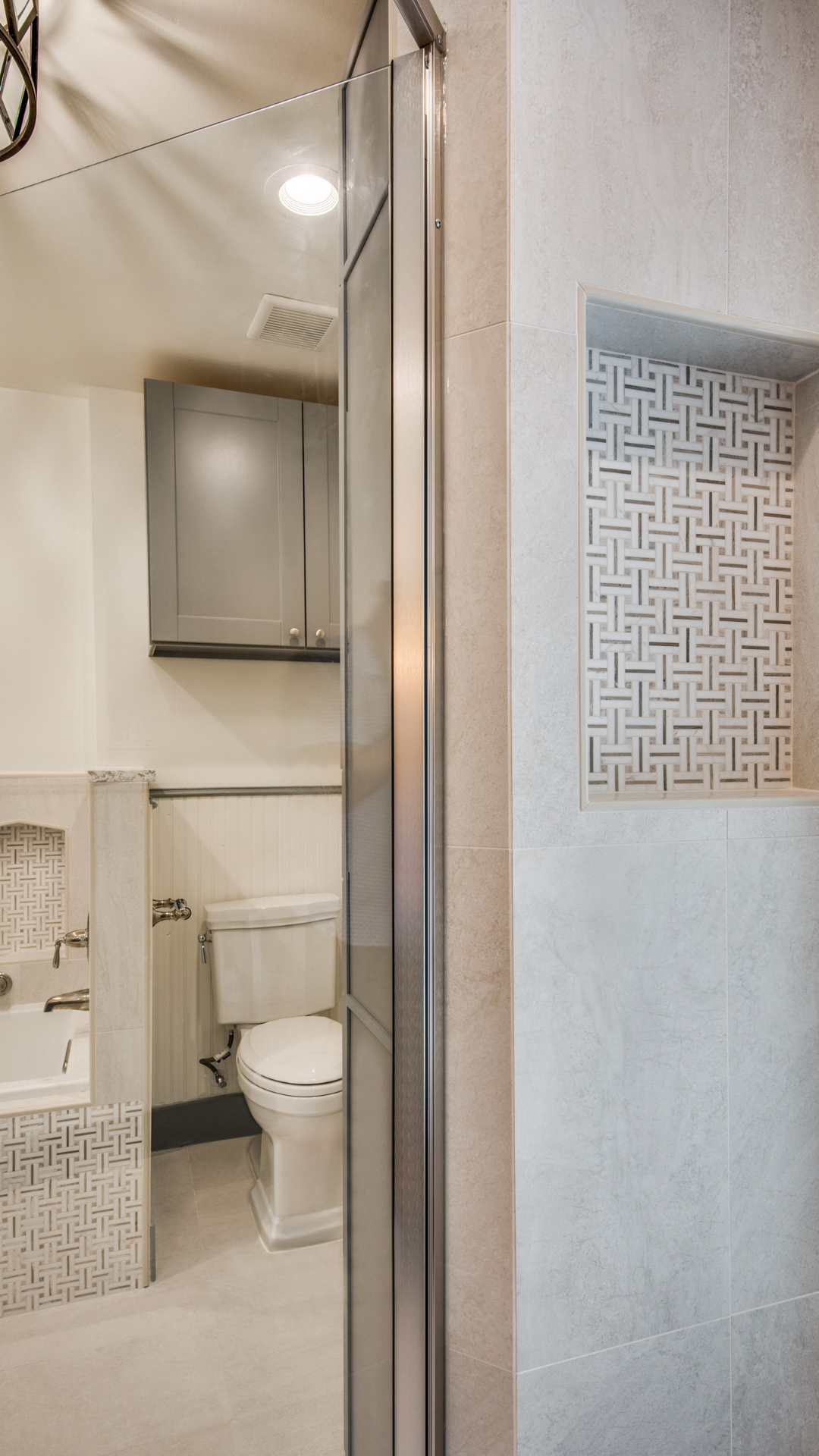 Bathroom with gray shower door, toilet, cabinet, and decorative wall niche with mosaic tiles.