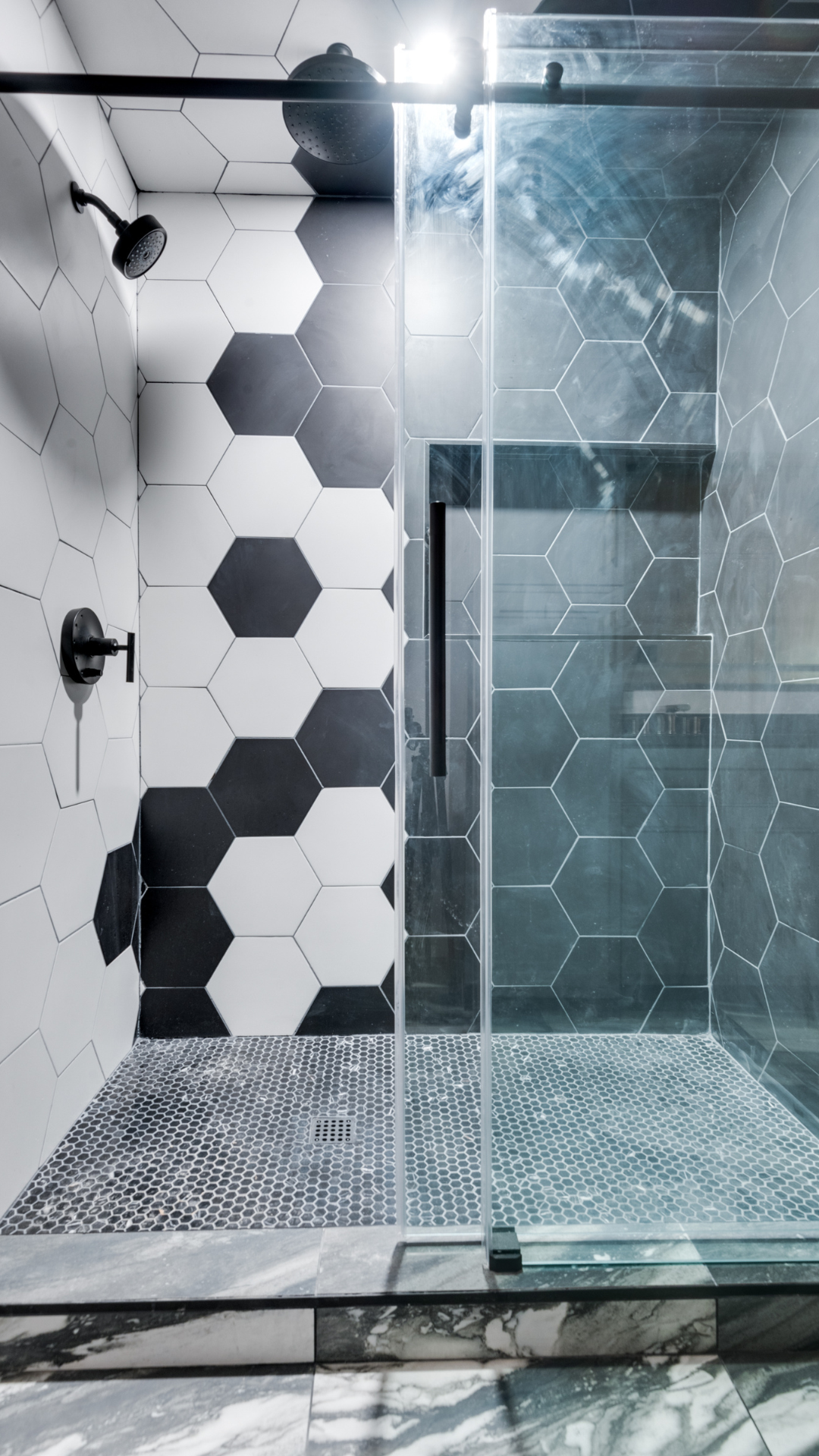 Modern shower with black and white hexagon tiles, glass door, and black fixtures.