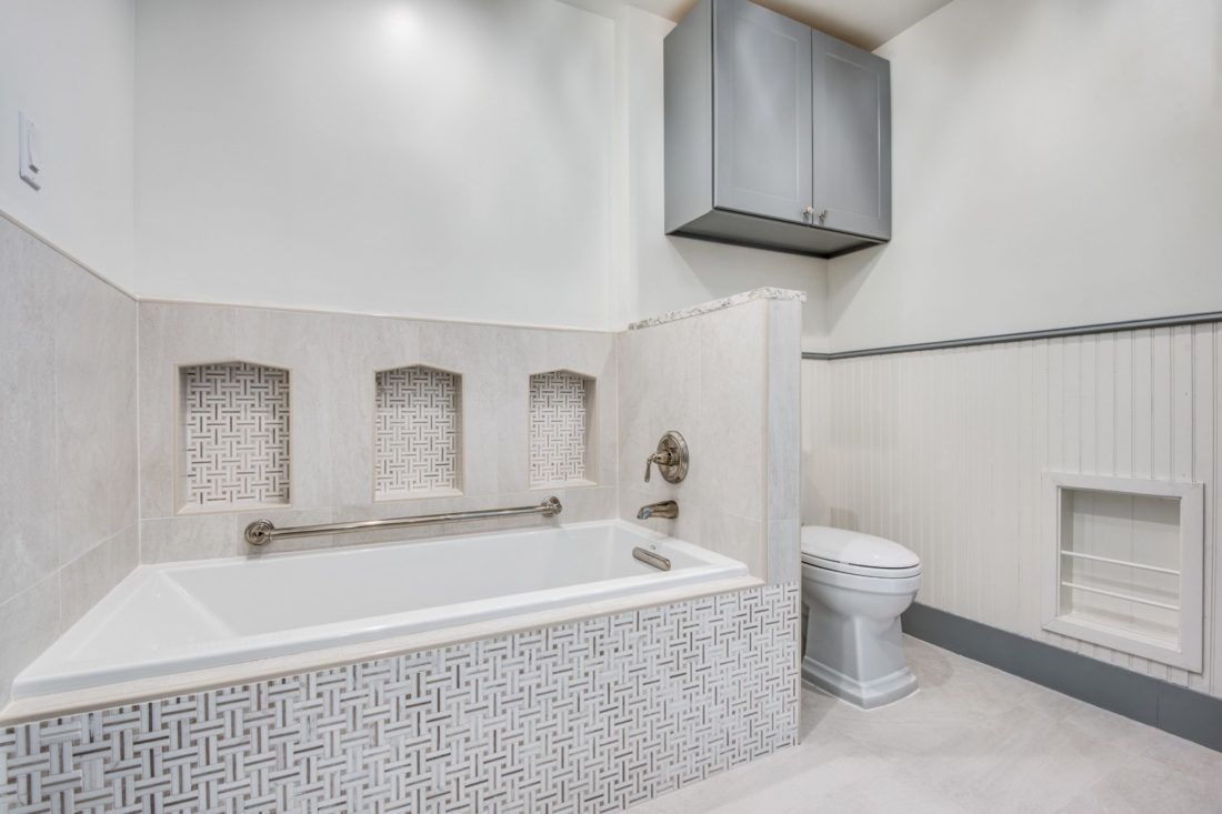 A bathroom with a bathtub , toilet and cabinets.