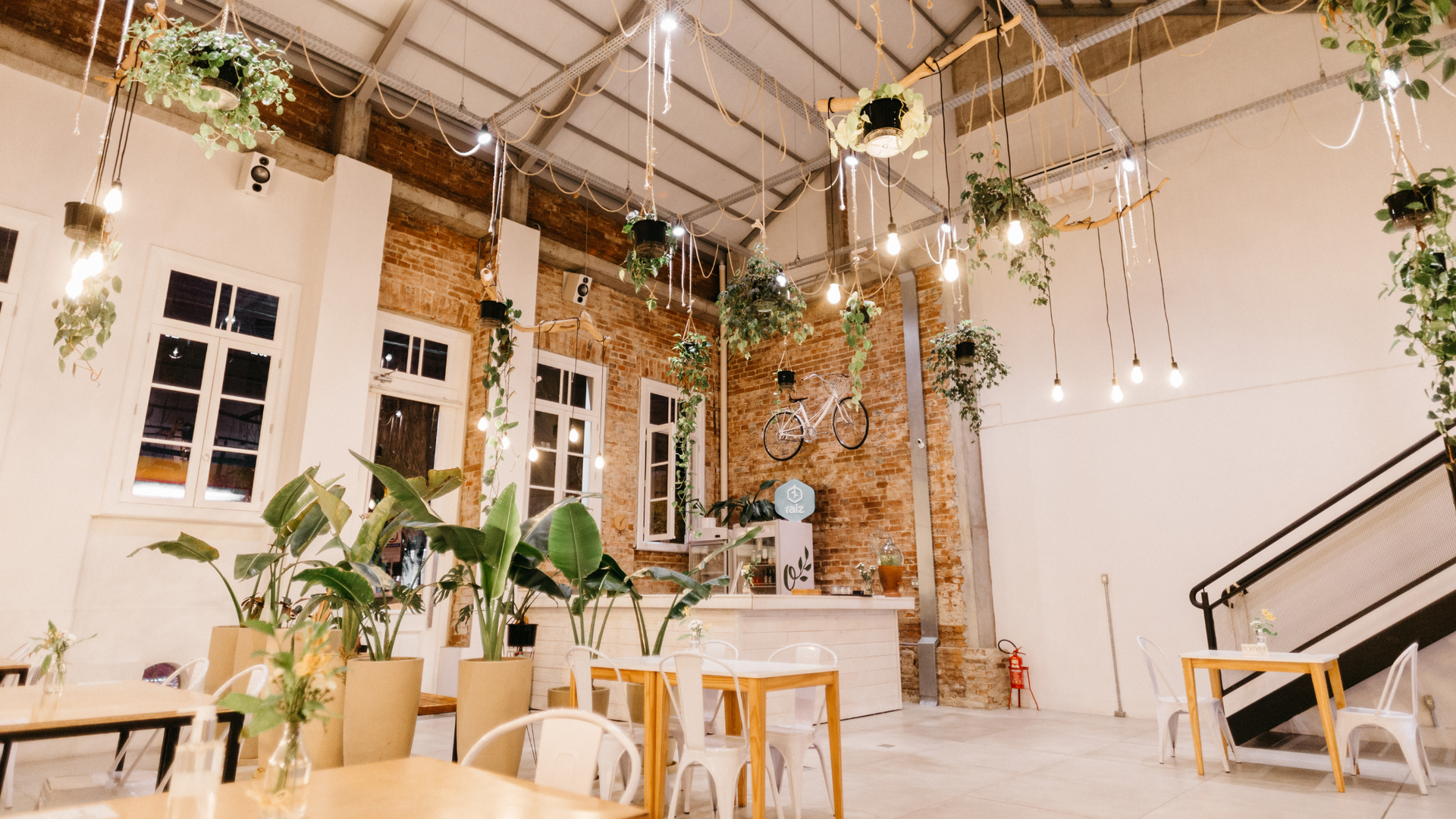 Indoor event space, brick walls, hanging plants, string lights, tables and chairs.